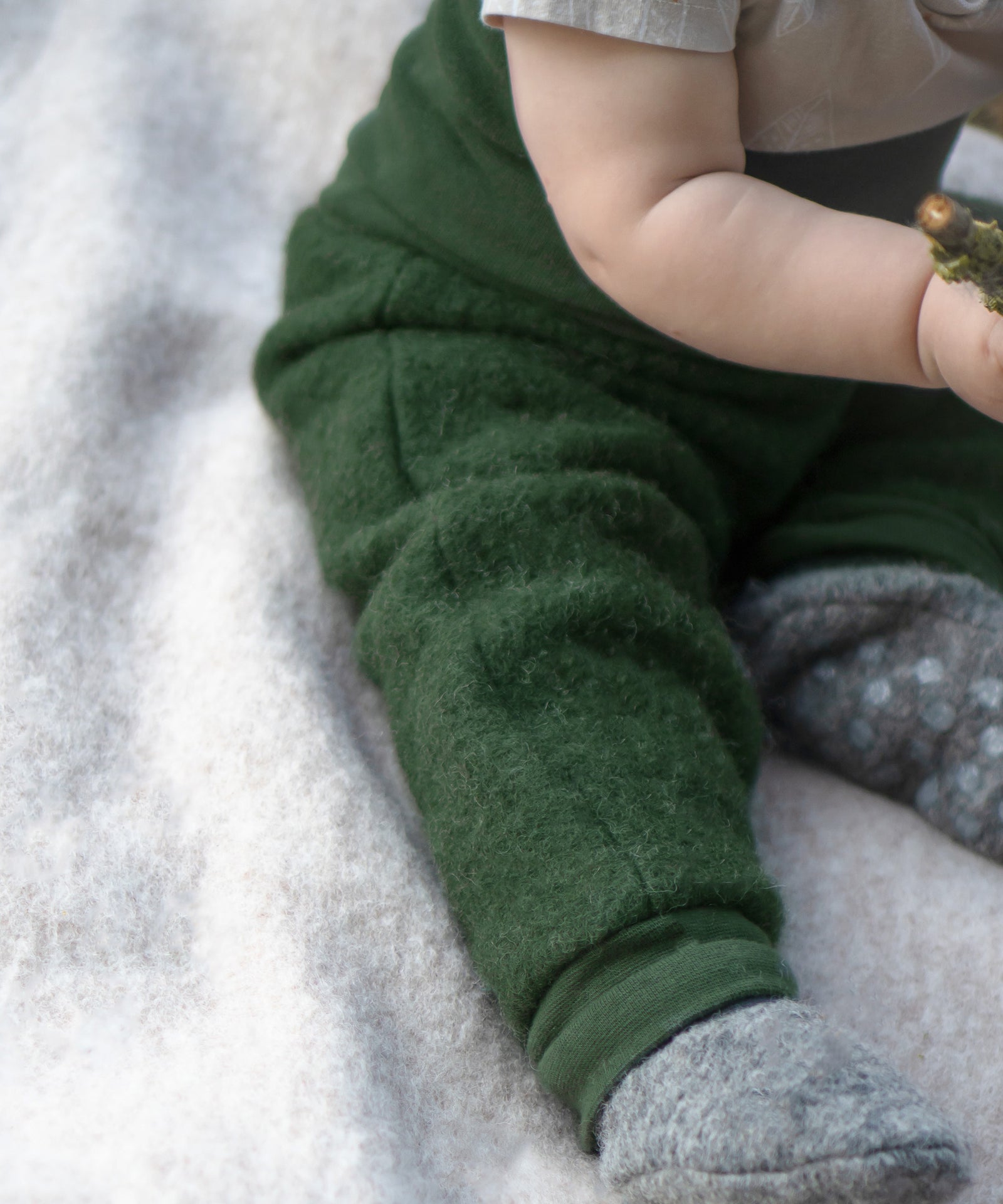 Atmungsaktiv & robust*Wolle kann Feuchtigkeit aufnehmen, ohne sich nass anzufühlen.
Das pflegeleichte Material ist von Natur aus schmutzabweisend.|Baby sitzt auf einer Walkdecke. Nahaufnahme der Walkhose.