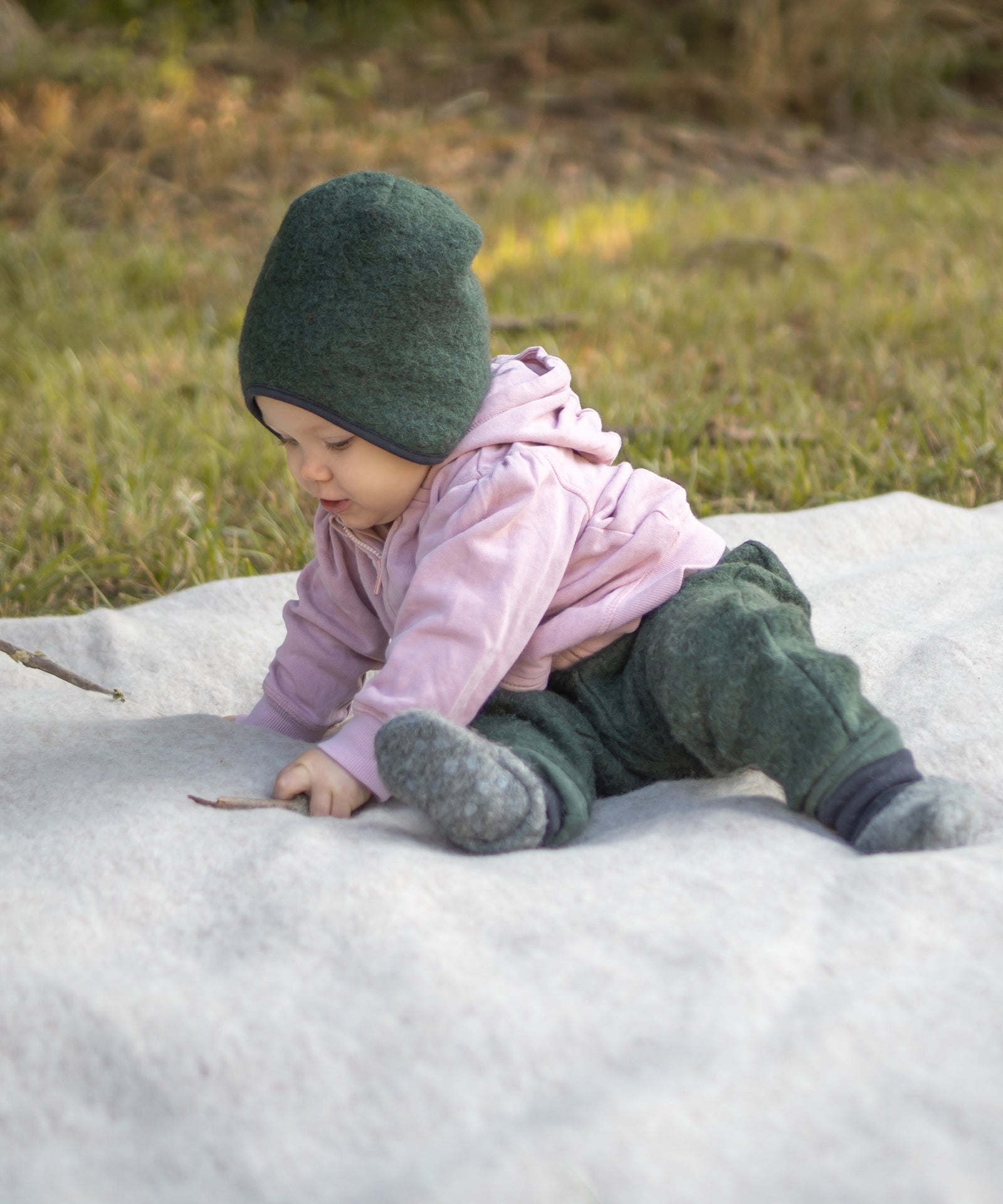 Baby sitzt auf einer Walkdecke und spielt mit Stöcken.