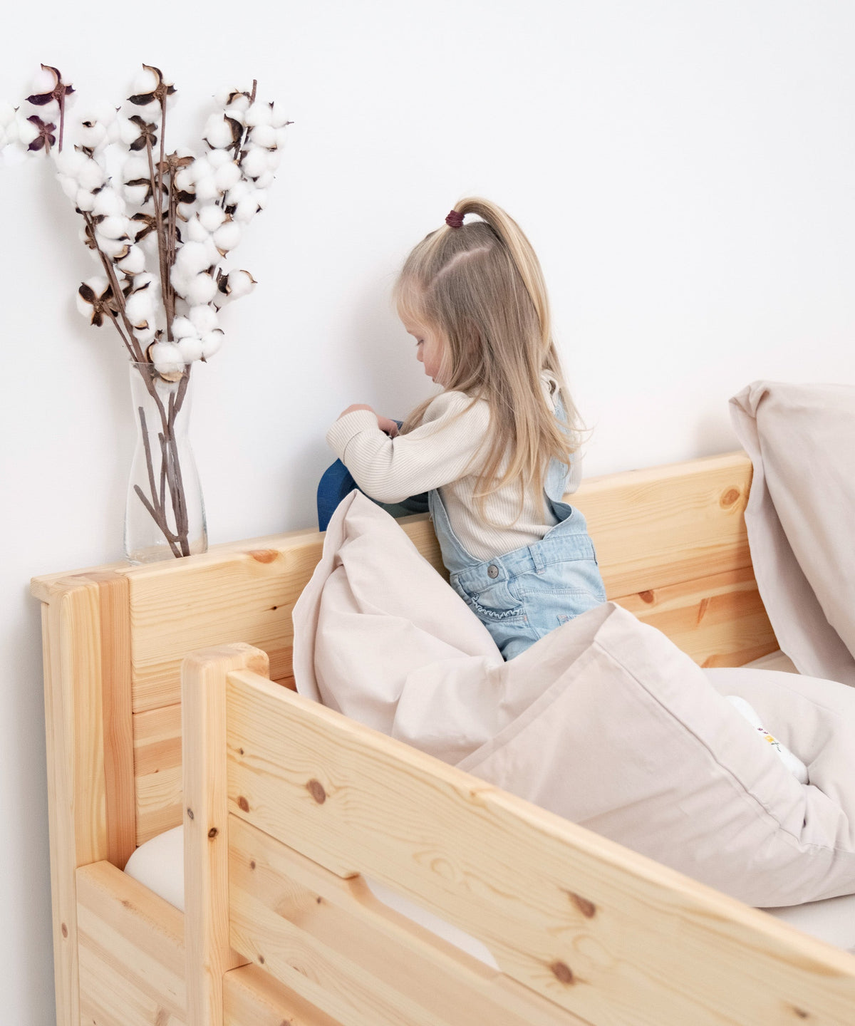 Mädchen spielt mit Holzspielzeug auf Ablage für Familienbett, Rausfallschutz ist am Bettrand angebracht.