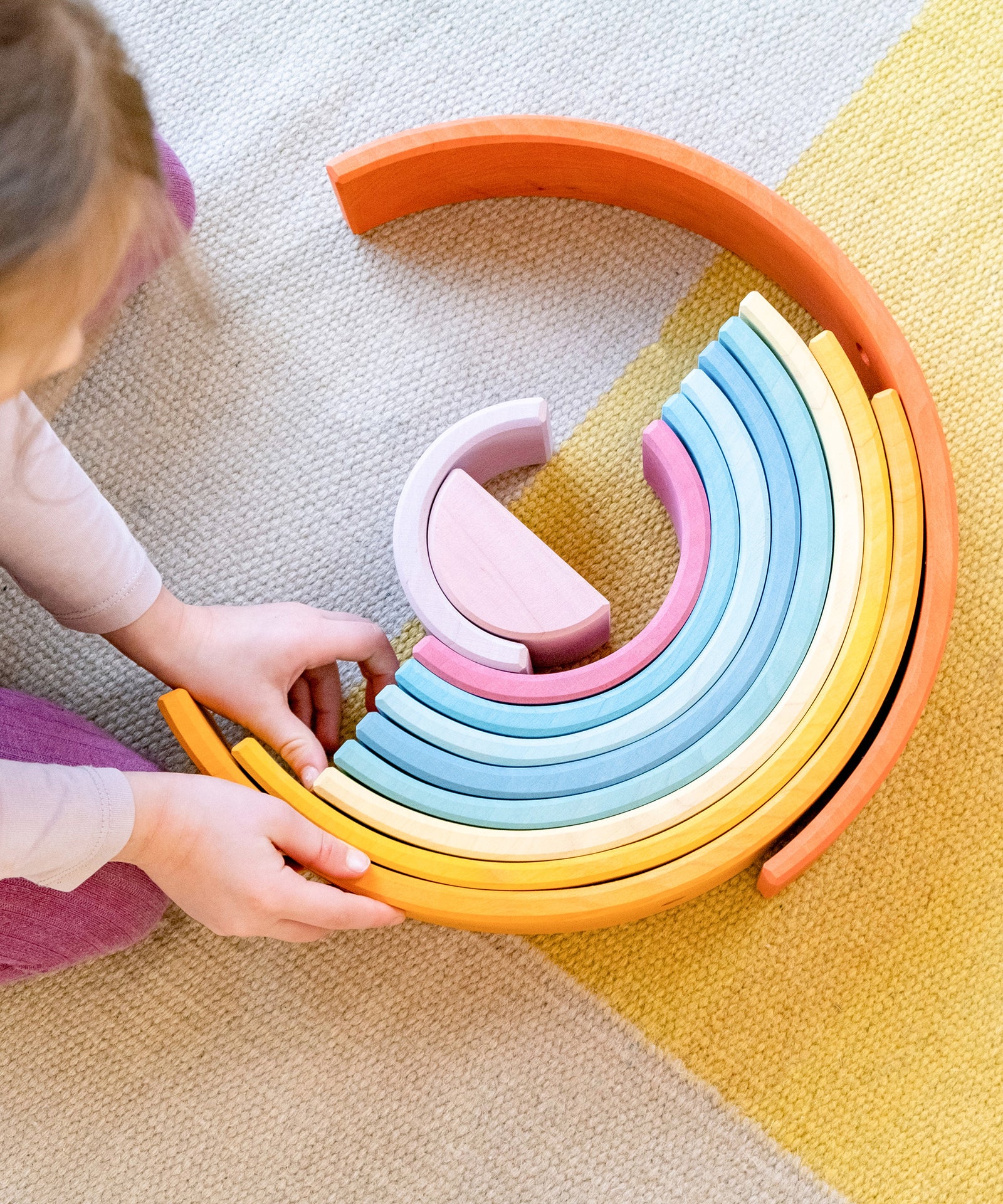 Hochwertig verarbeitet*Der Regenbogen besteht aus leichtem und gleichzeitig robustem Erlenholz aus nachhaltiger Forstwirtschaft.|Mädchen baut Turm aus Bogenelementen des Regenbogens natur.