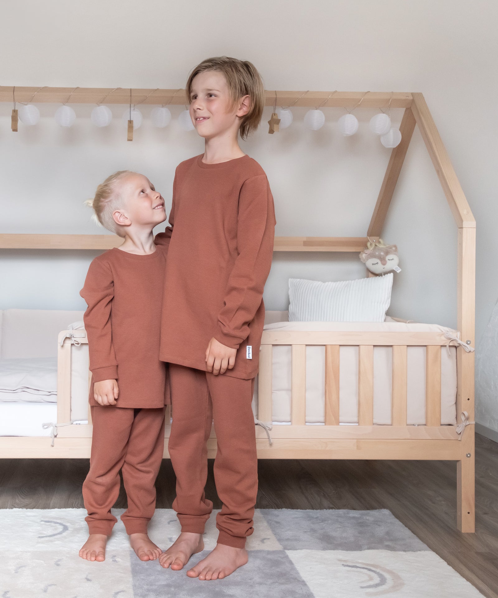 Schöne Farben & Designs*Der Schlafanzug ist in sechs zeitlosen Designs und drei hochwertigen Qualitäten, Interlock, Rippe und Waffelstruktur, erhältlich.|Zwei Kinder mit Kinderschlafanzug Rost Waffel.