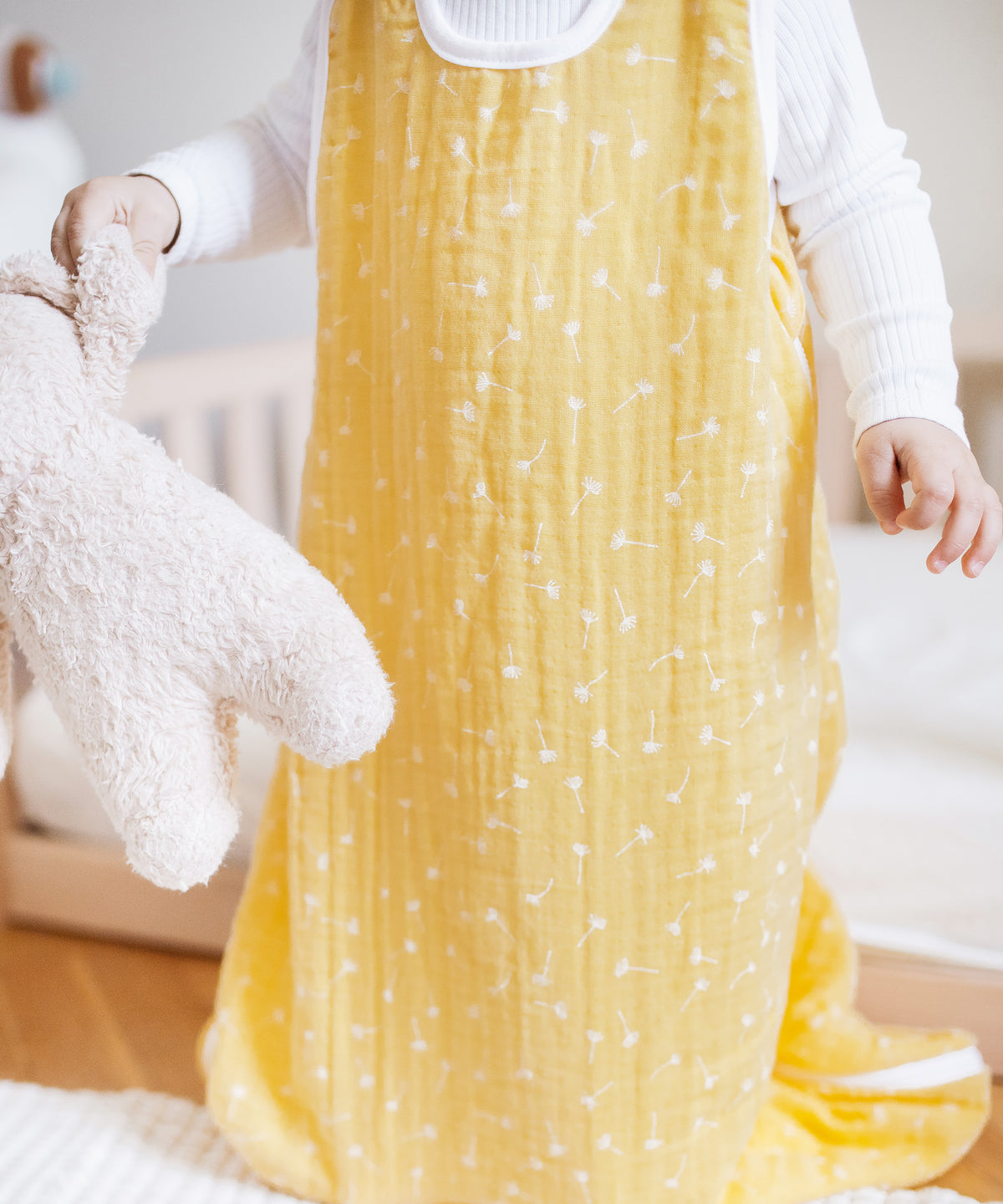 Baby mit Schlafsack aus Musselin mit Teddy in der Hand.