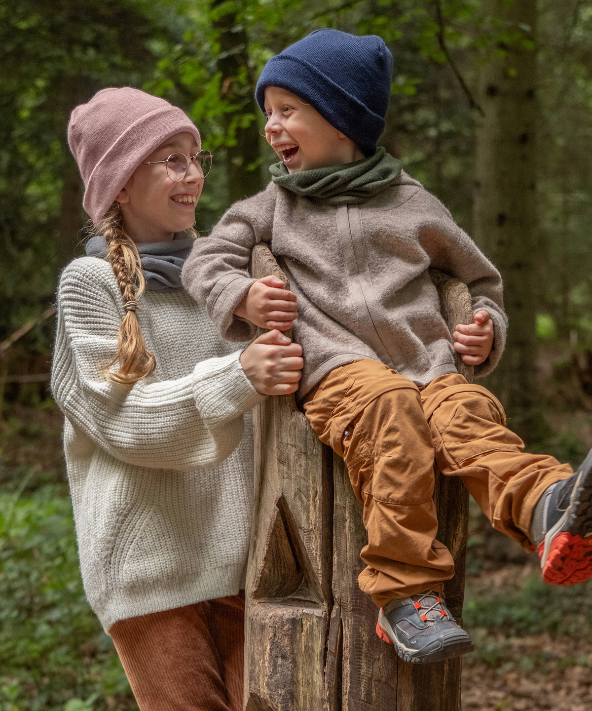 Zwei Kinder mit Schlauchschal und Strickmütze im Wald.