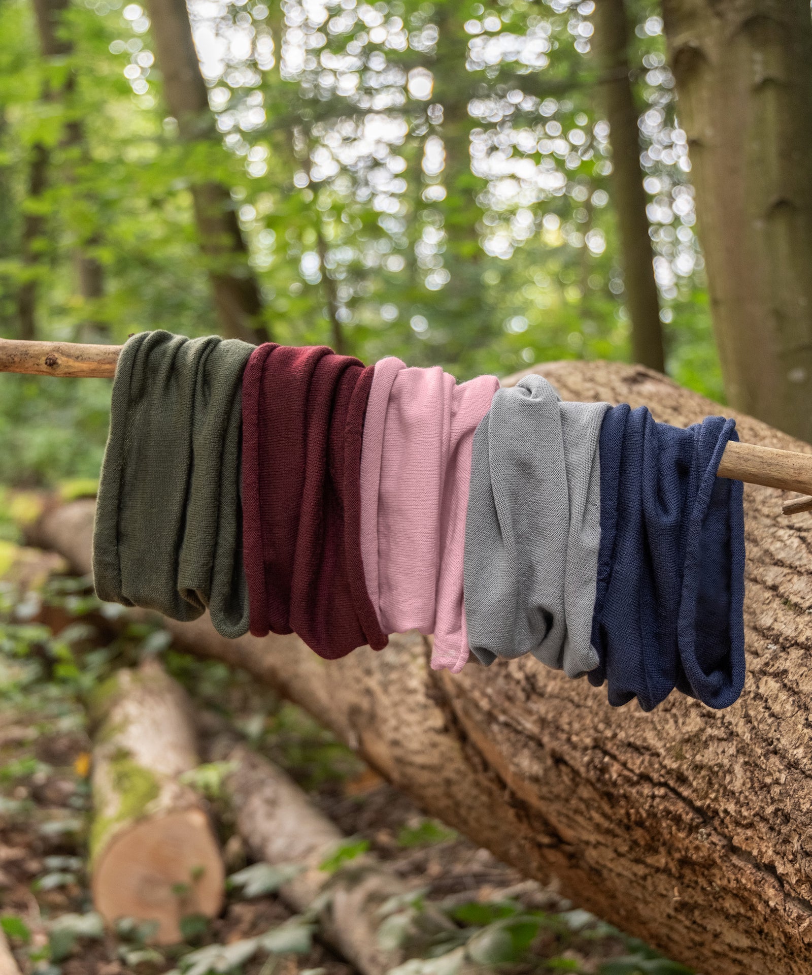 Nachhaltig*Die extrafeine Schurwolle für den Loopschal ist mulesingfrei und stammt aus kontrolliert biologischer Tierhaltung (k.b.T.).|Schlauchschals in fünf Farben hängen nebeneinander an einem Zweig.