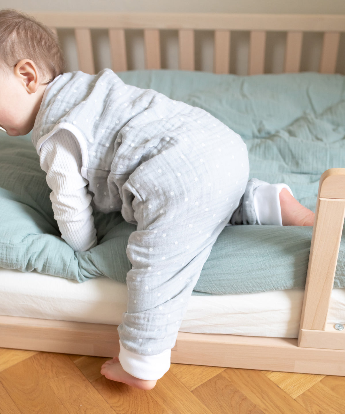 Baby mit Musselin Sommerschlafsack mit Beinen steigt aus Bodenbett.