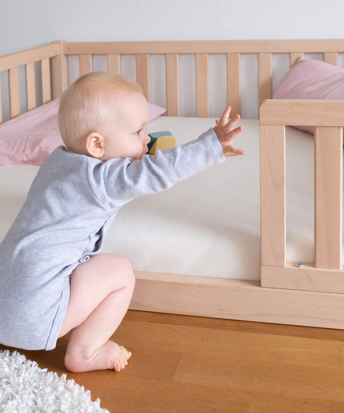 Baby vor Bodenbett mit Spannbettlaken.