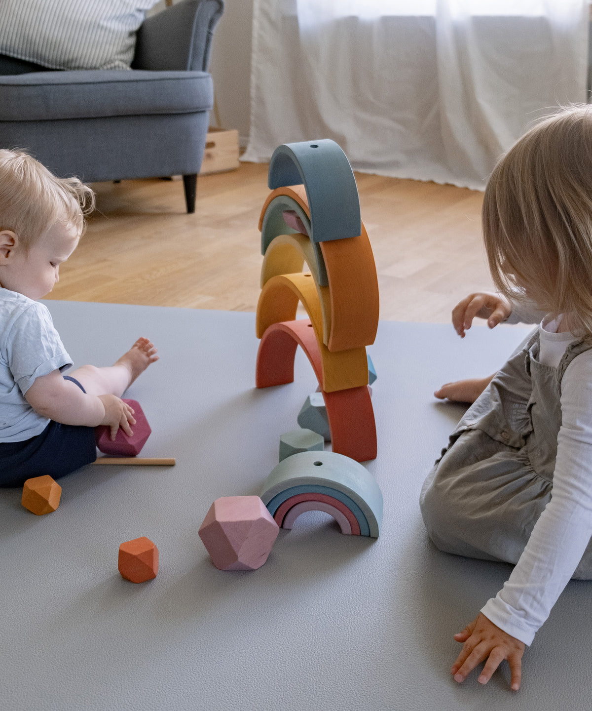 Zwei Kinder spielen mit Holzspielzeug auf Krabbelmatte Pro hellgrau.