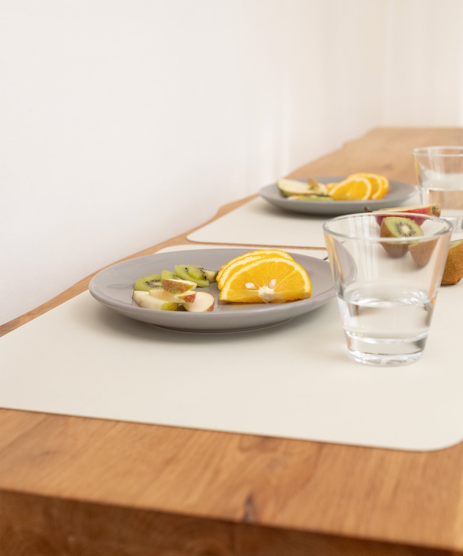 Zwei Teller mit Obst und Gläsern auf Tischsets, die stilvoll die Tischoberfläche schützen.