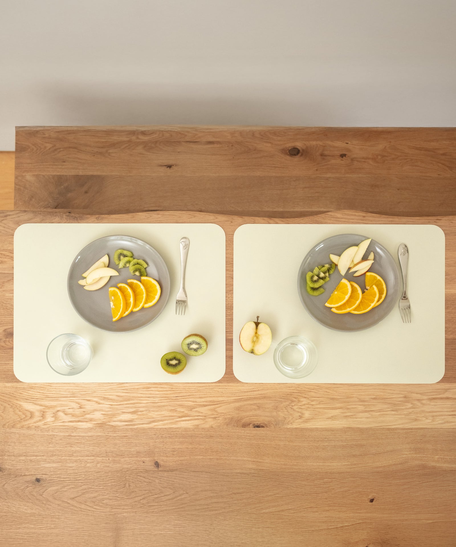Perfekte Unterlage beim Essen*Das Tischset ist der optimale Schutz für deinen Esstisch - erhältlich in zwei Größen als praktisches 2er-Set und 4er-Set.|Zwei Tischsets schützen die Holzoberfläche, jedes mit einem Teller voller Obst und einem Glas Wasser.