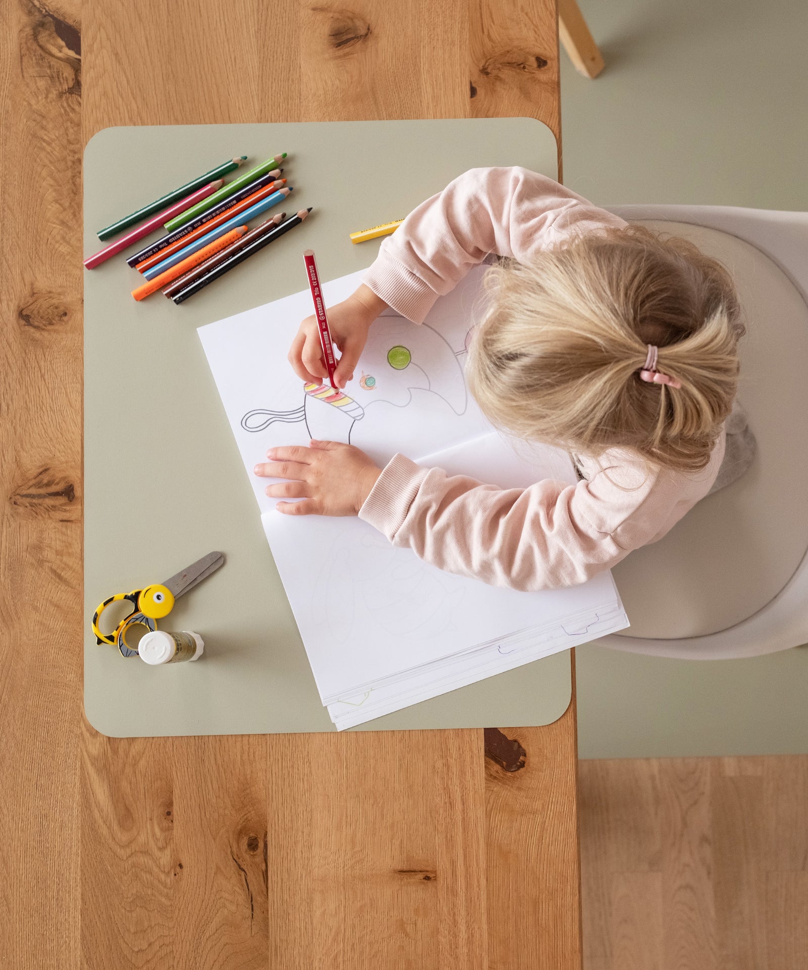 Ein Kind malt auf einem Tischset, das als Bastelunterlage dient.