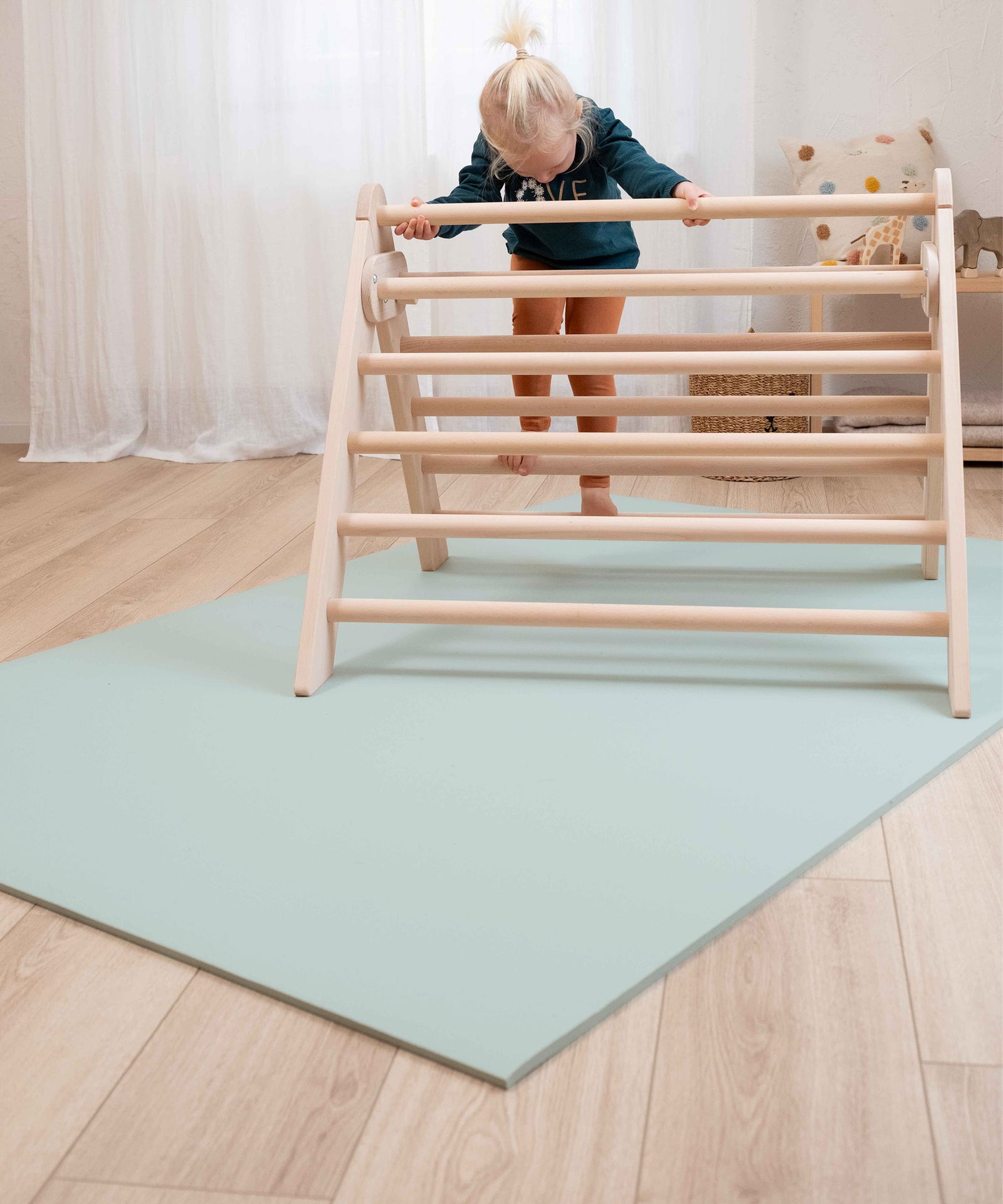 Schützende Funktion*Als Zwischenlage unter Krabbelmatten oder Teppichen schützt das Vlies empfindliche Böden mit behandelten Oberflächen und Steinböden.|Kind klettert auf ein Kletterdreieck, das auf einer Krabbelmatte steht.