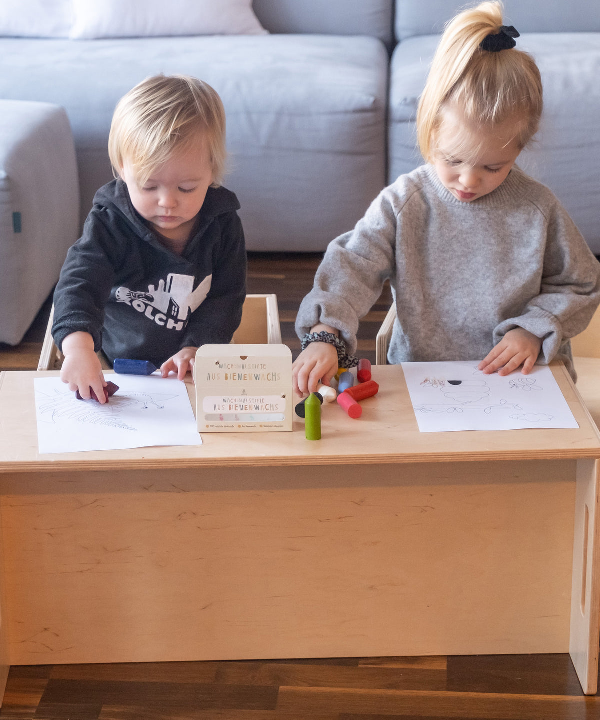 Zwei Kinder sitzen nebeneinander und malen mit den Wachsmalstiften Bilder aus.