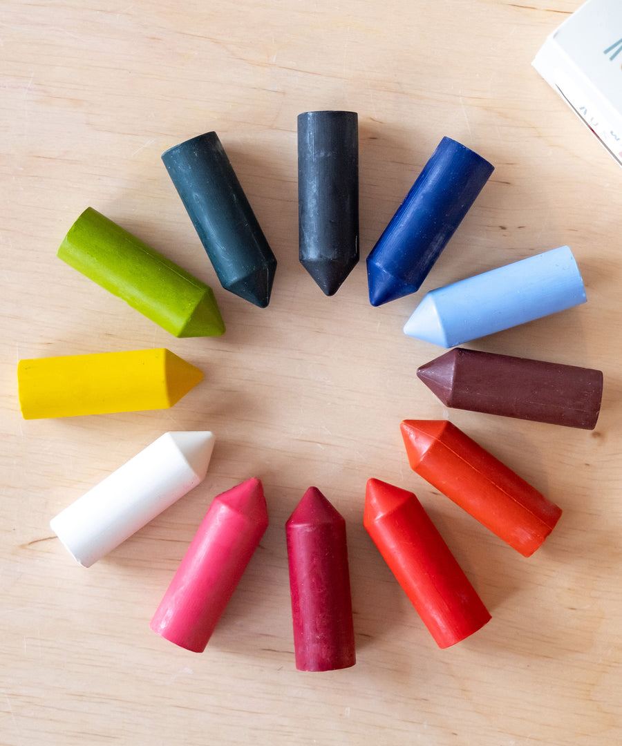 Die Wachsmalstifte in zwölf verschiedenen Farben liegen im Kreis aufgereiht auf dem Tisch.