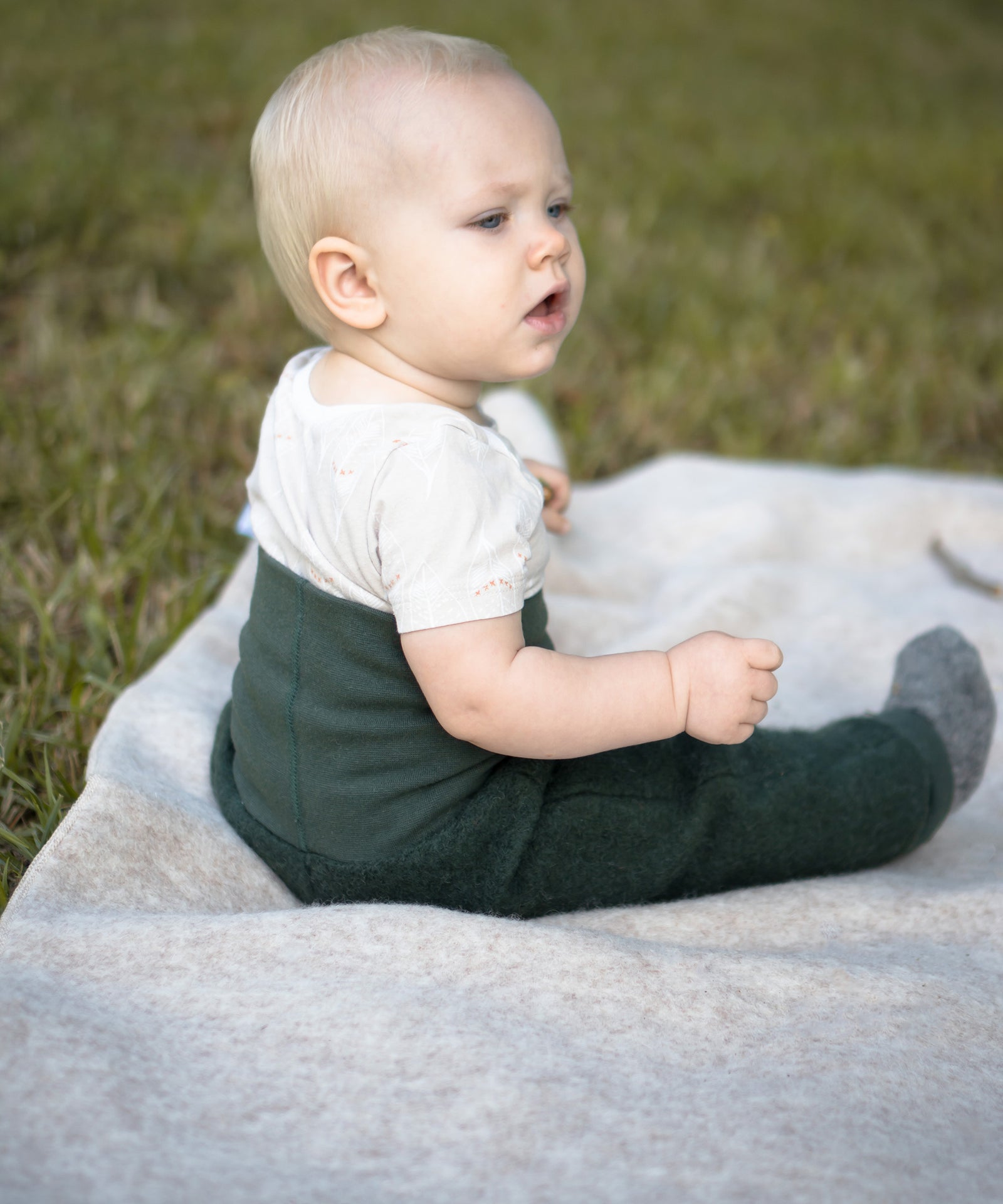 Baby sitzt auf einer Walkdecke.