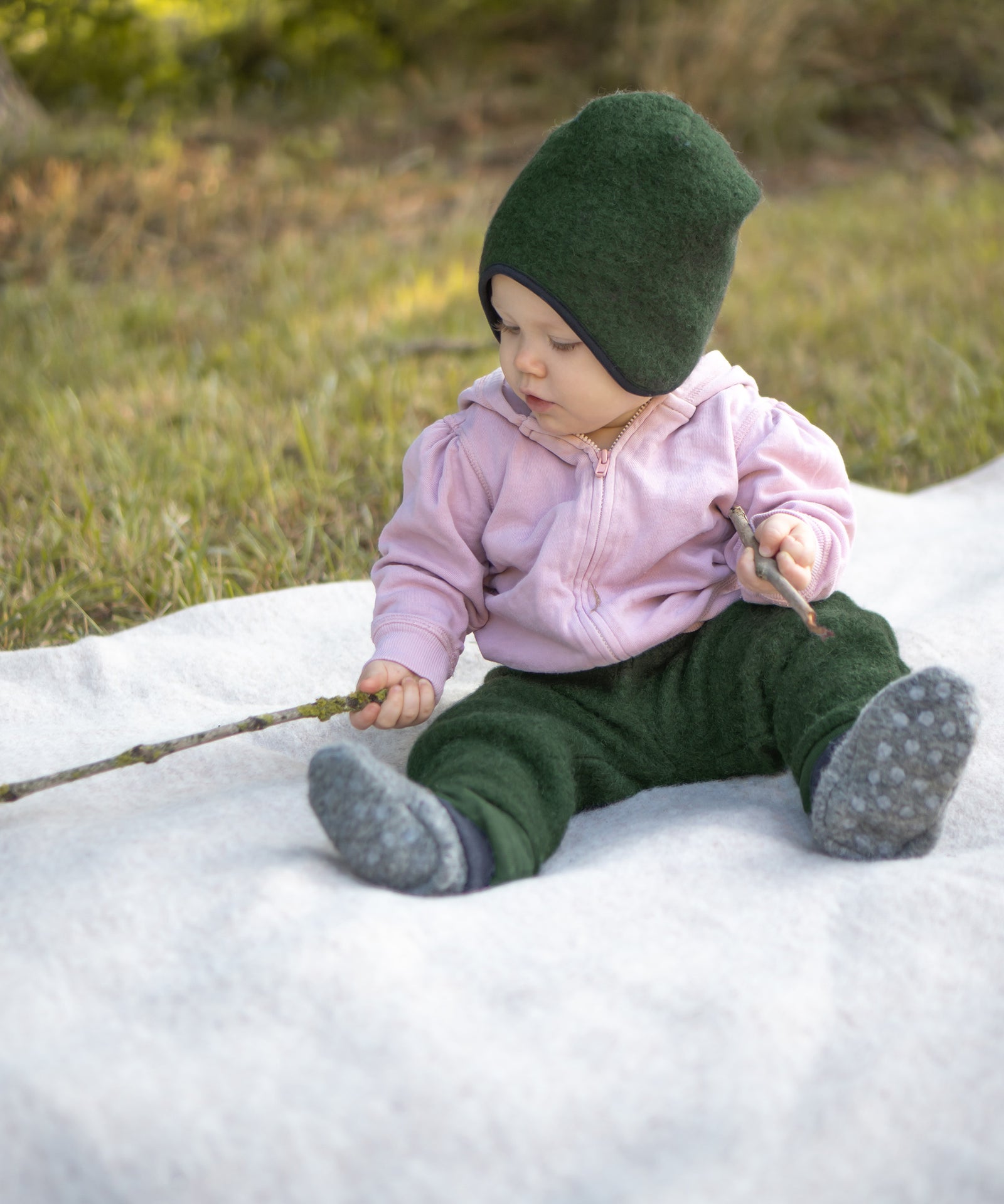 Baby sitzt auf einer Decke und spielt mit Stöcken.