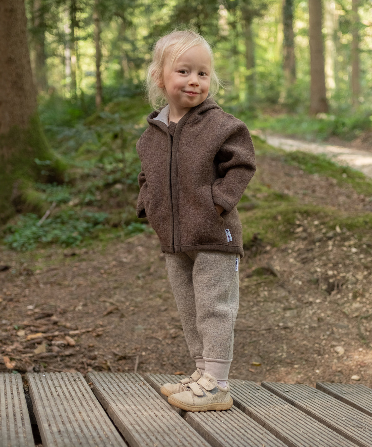 Kind mit Walk Hose und Walkjacke steht im Wald.