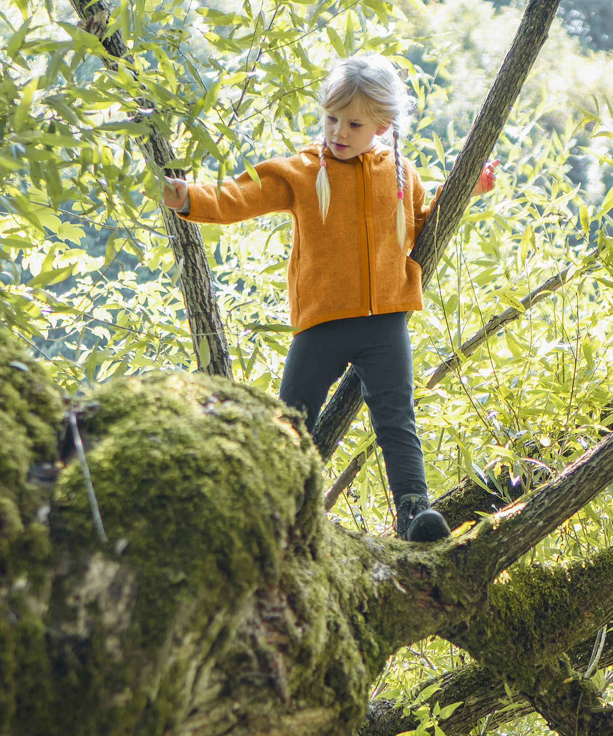 Kind mit Walkjacke in safrangelb steht in Baum.