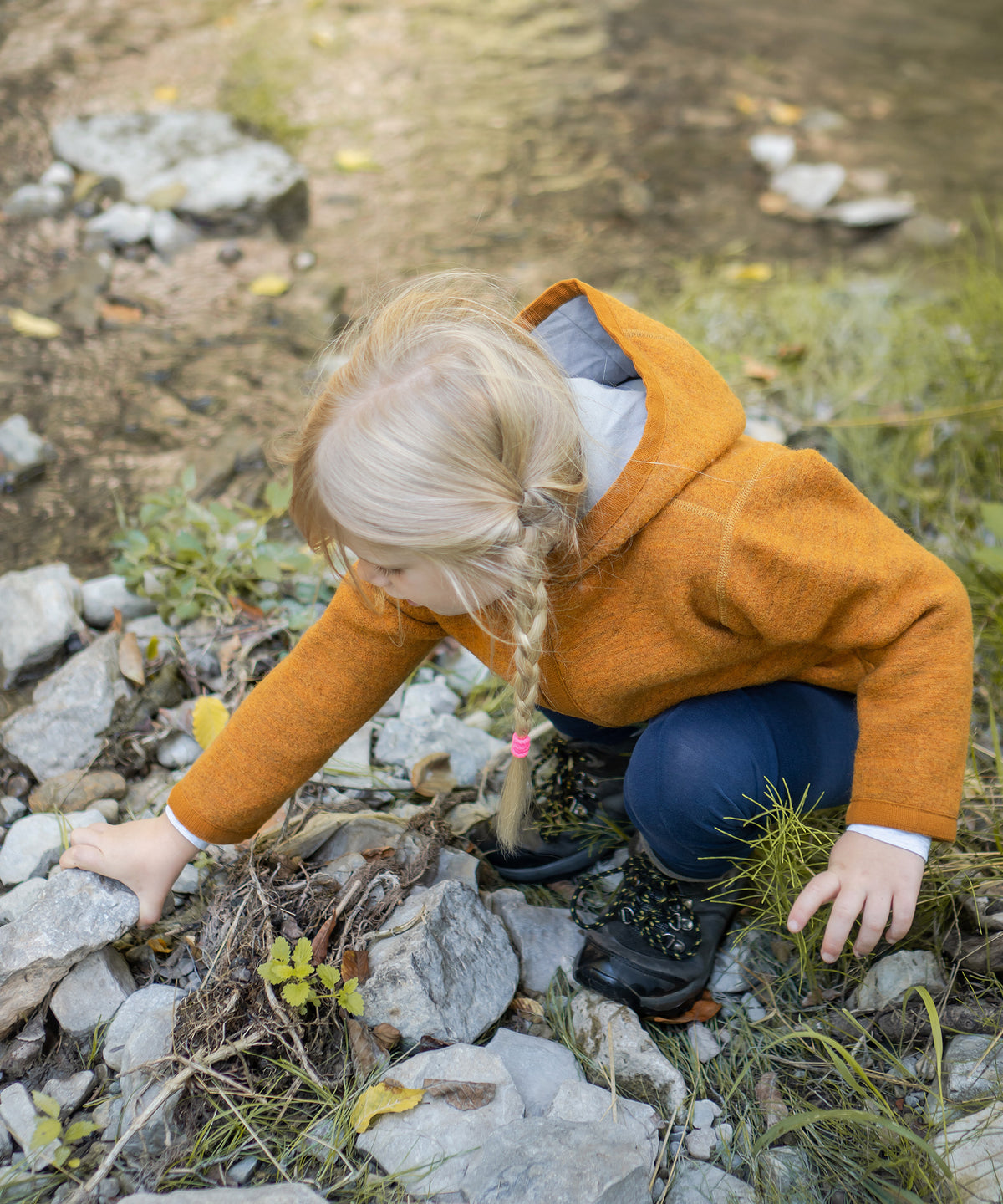 Kind mit Walkjacke in safrangelb spielt mit Seinen am Bach.