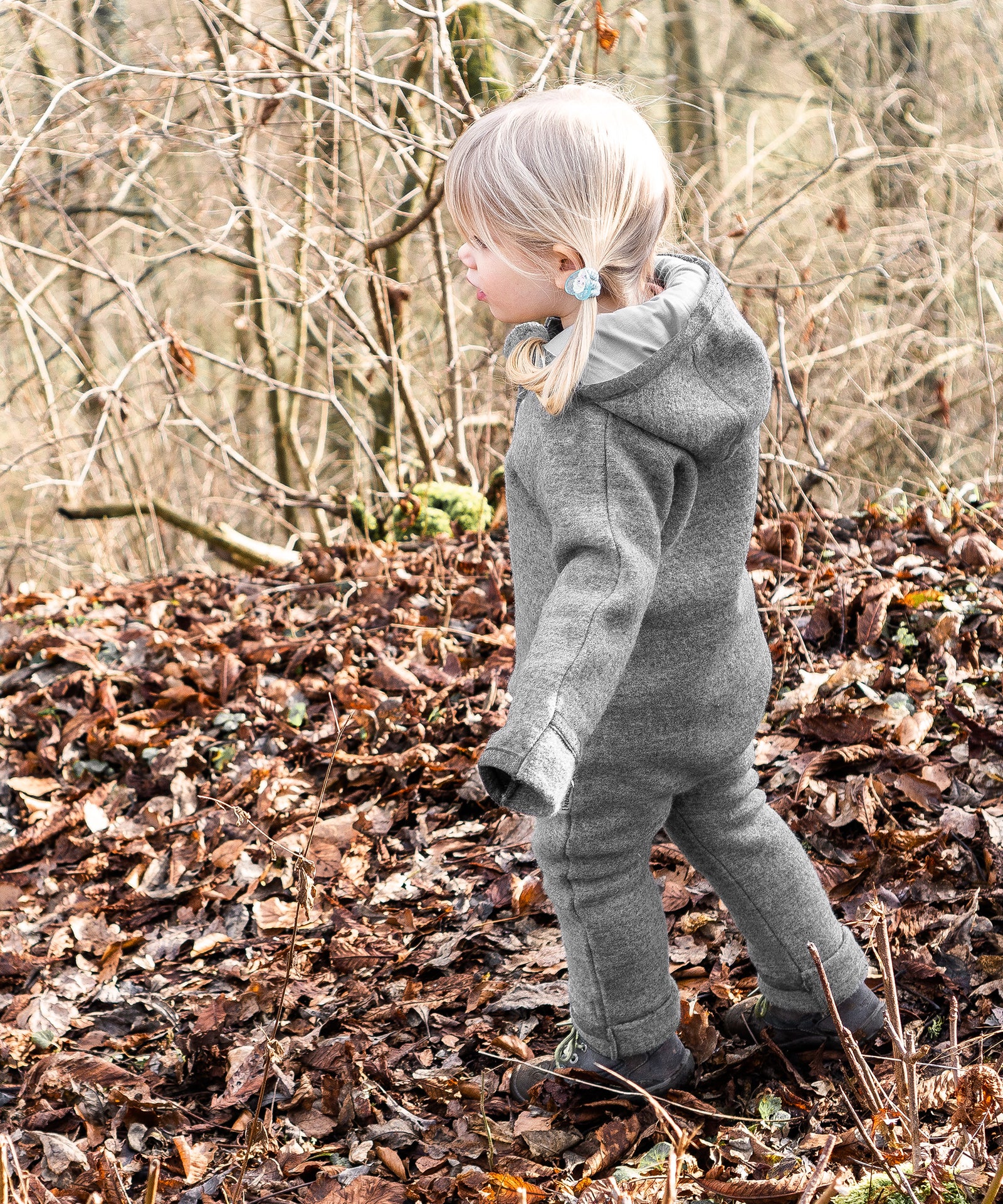 Mädchen mit atmungsaktivem Walkoverall in Grau steht im Wald.