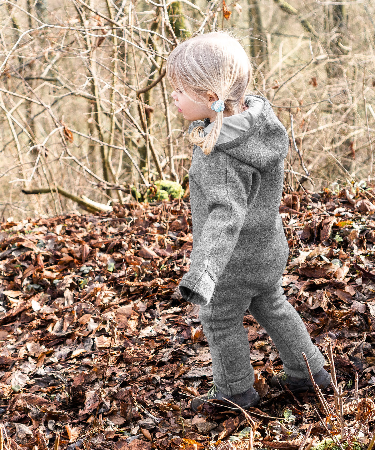 Mädchen mit atmungsaktivem Walkoverall in Grau steht im Wald.