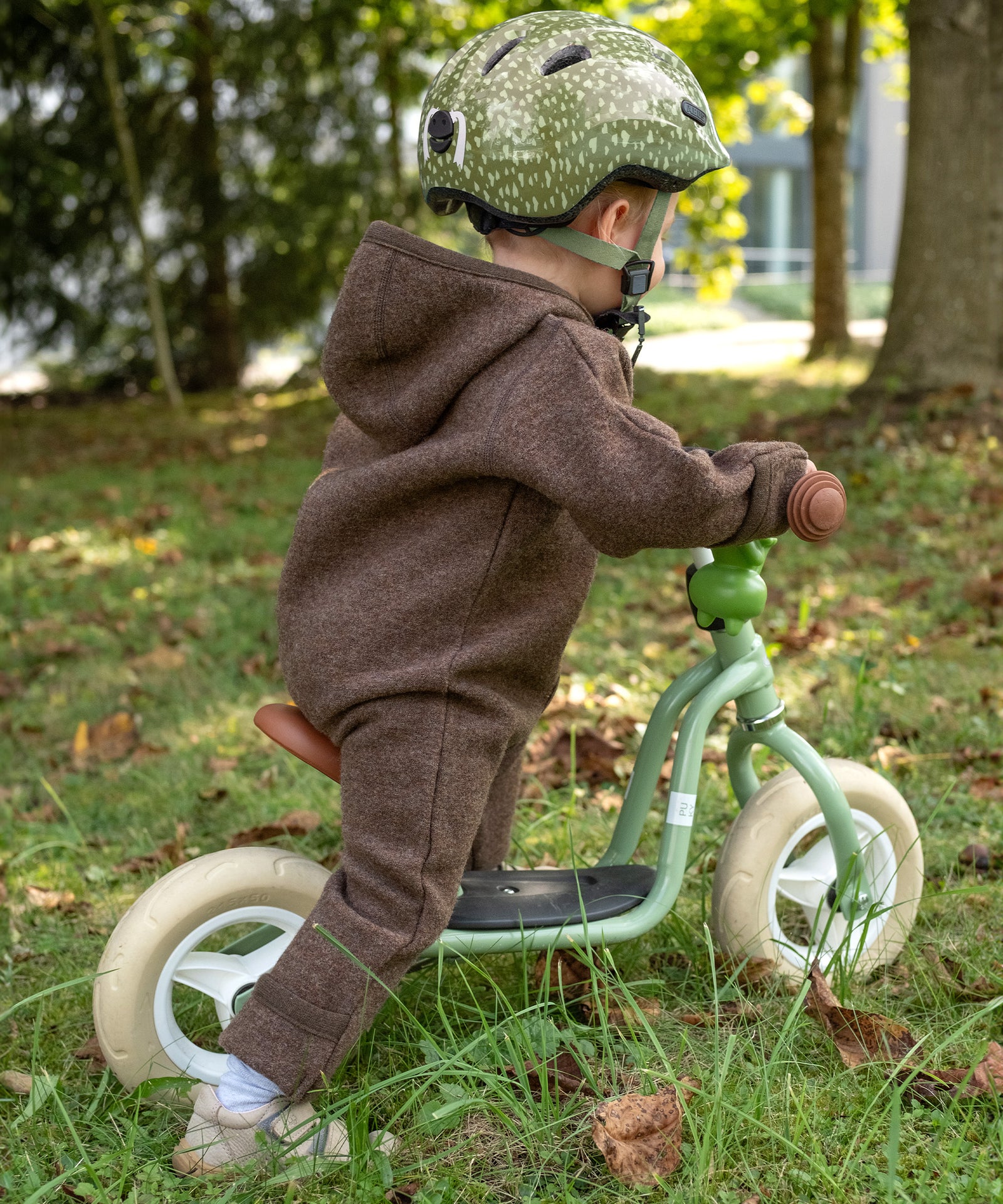Kind im Walkoverall fährt auf einem Laufrad.