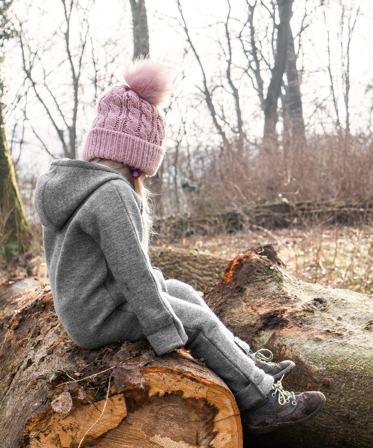 Mädchen mit Walkoverall sitzt auf Baumstamm.