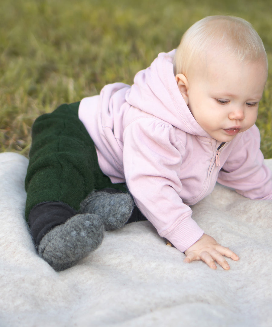Nachhaltig produziert*Die ausgeklügelte Mischung aus 80% mulesingfreier Bio-Schurwolle und 20% Bio-Baumwolle macht die Walkschühchen extra bequem.|Baby sitzt auf einer Walkdecke.