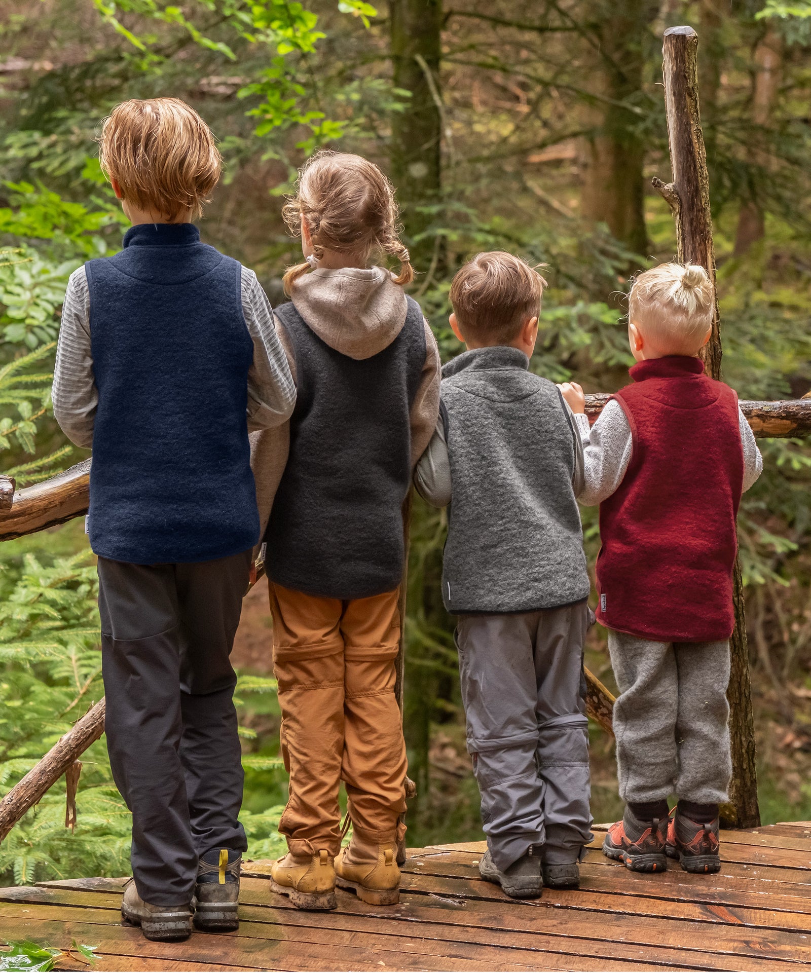 Bequeme Passform*Die Walkweste bietet Bewegungsfreiheit beim Spielen & Klettern. Sie ist so geschnitten, dass Bauch & Rücken dabei schön warm bleiben.|Rückansicht von Kindern mit Walkwesten in vier verschiedene Farben im Wald.