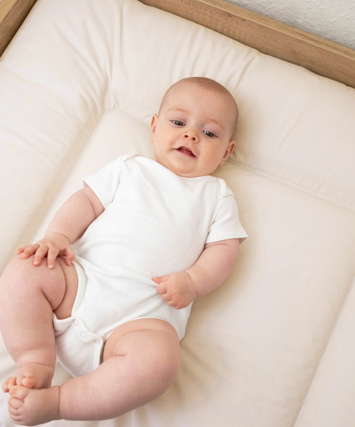 Baby liegt auf abwaschbarer Wickelauflage 72x85 cm in beige.