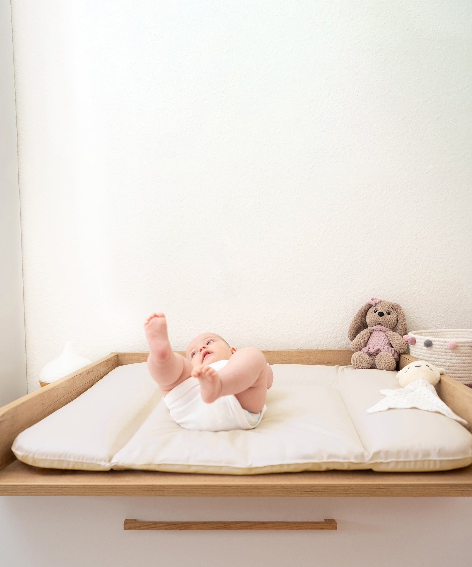 Baby liegt auf Wickeltisch mit Wickelauflage beige in Größe 72x85 cm.