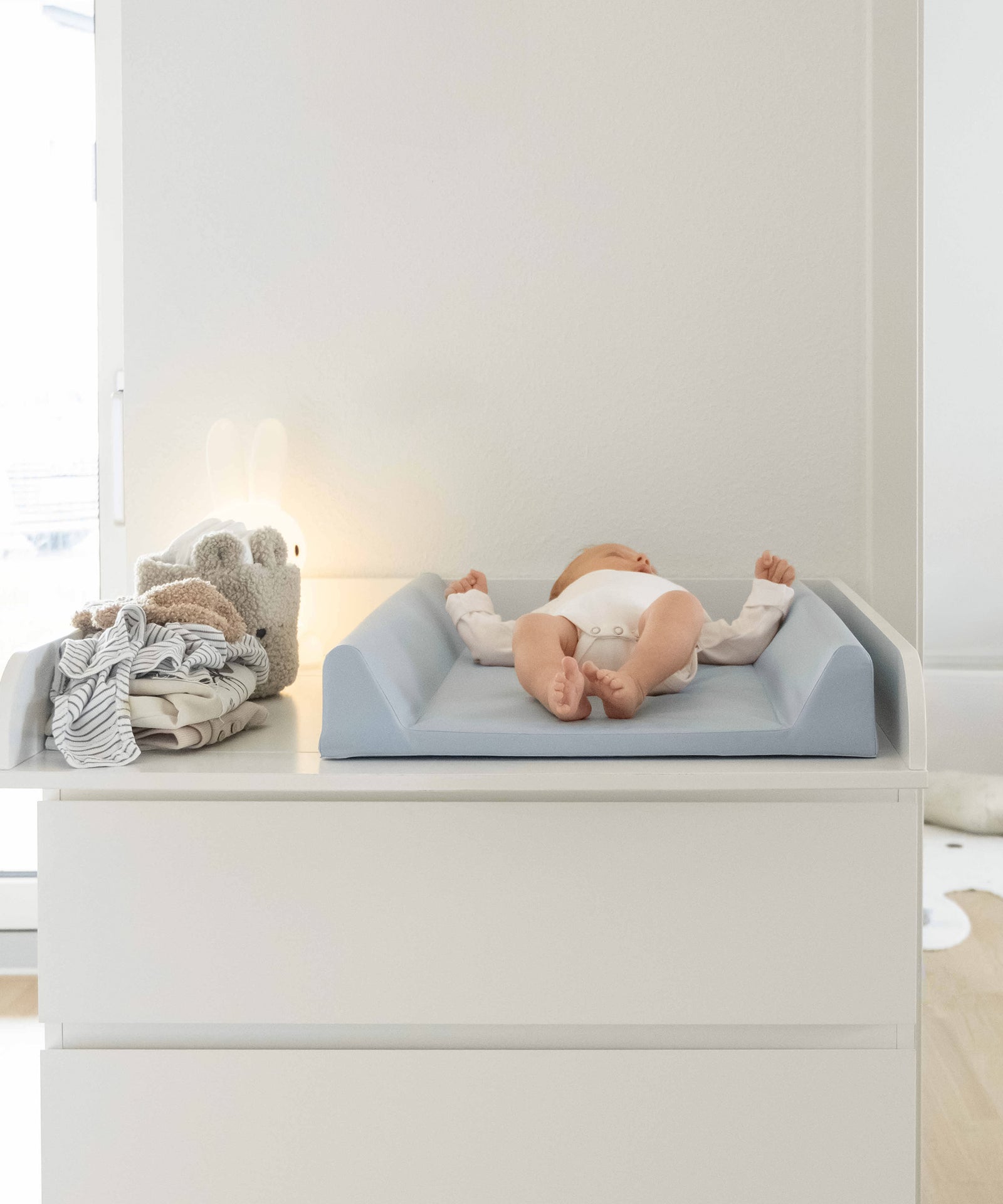 Baby auf hellblauer, abwaschbarer Wickelauflage 50x70 cm mit keilförmigen, erhöhten Seitenrändern.