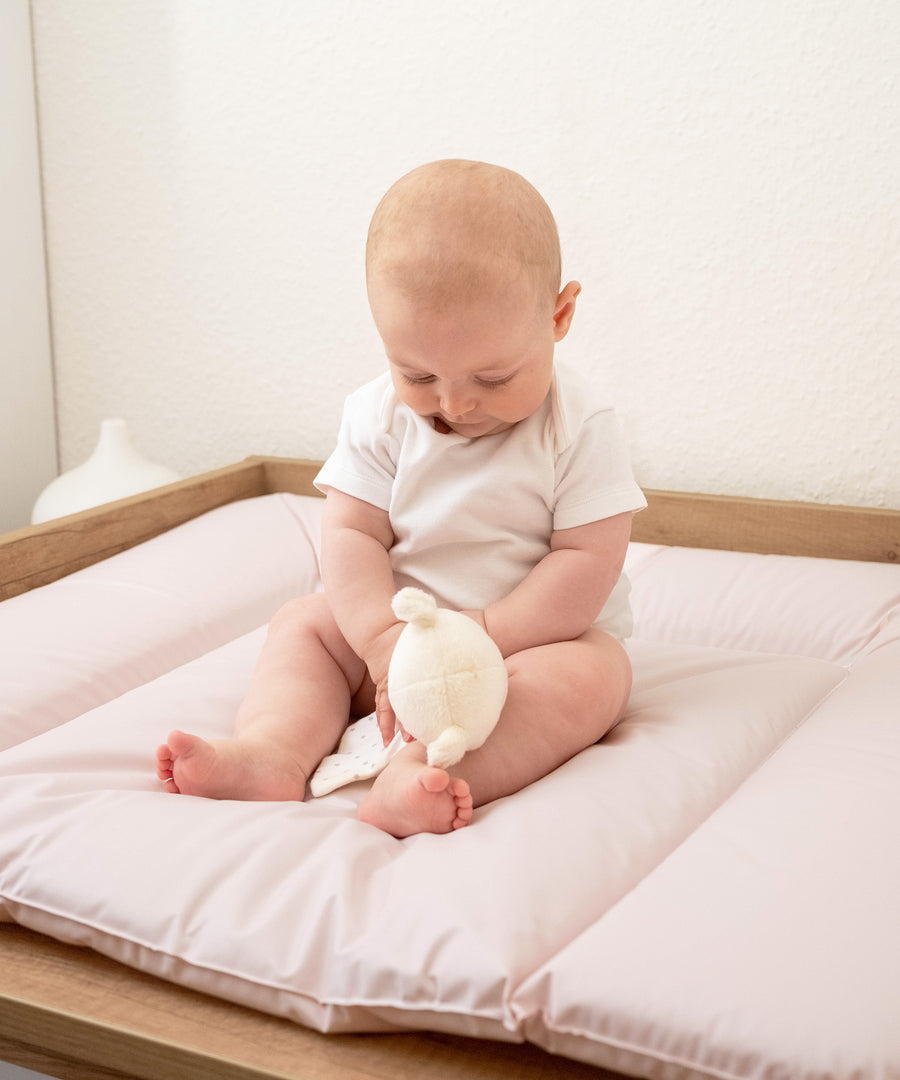 Baby sitzt auf weich gepolsterter Wickelunterlage in beige.