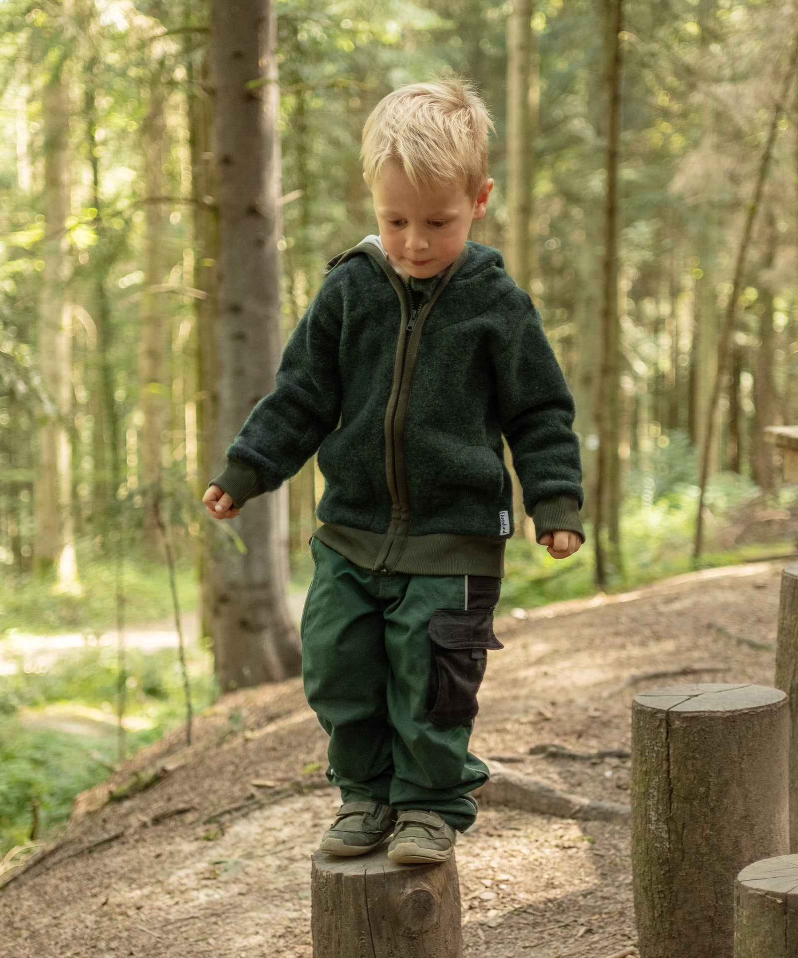 Junge mit atmungsaktiver Wollfleecejacke spielt im Wald.