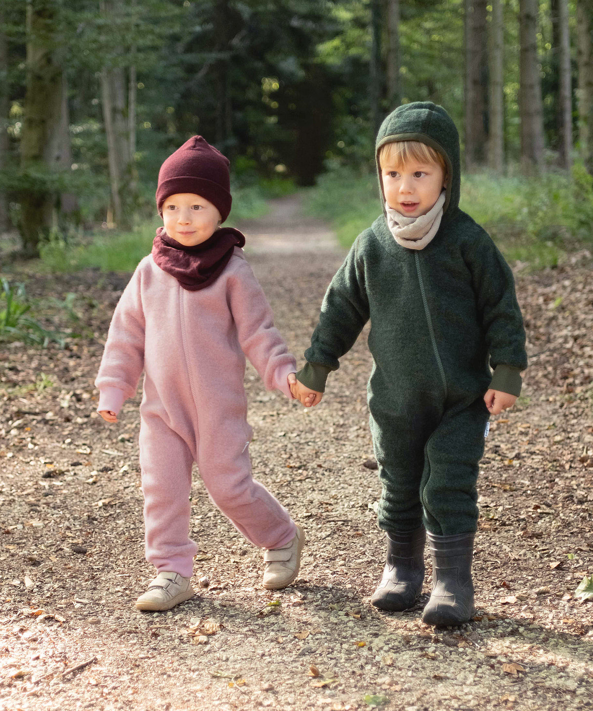 Zwei Kinder mit Wollfleece-Overalls gehen im Wald spazieren.