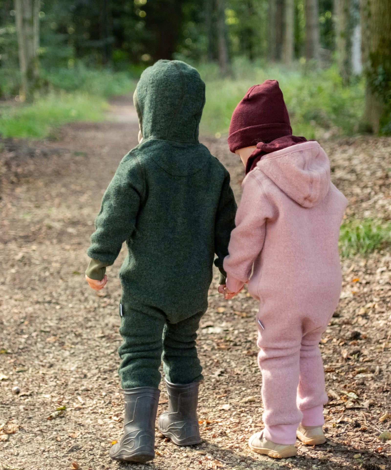 Zwei Kinder mit Wollfleeceoverall auf Waldweg.