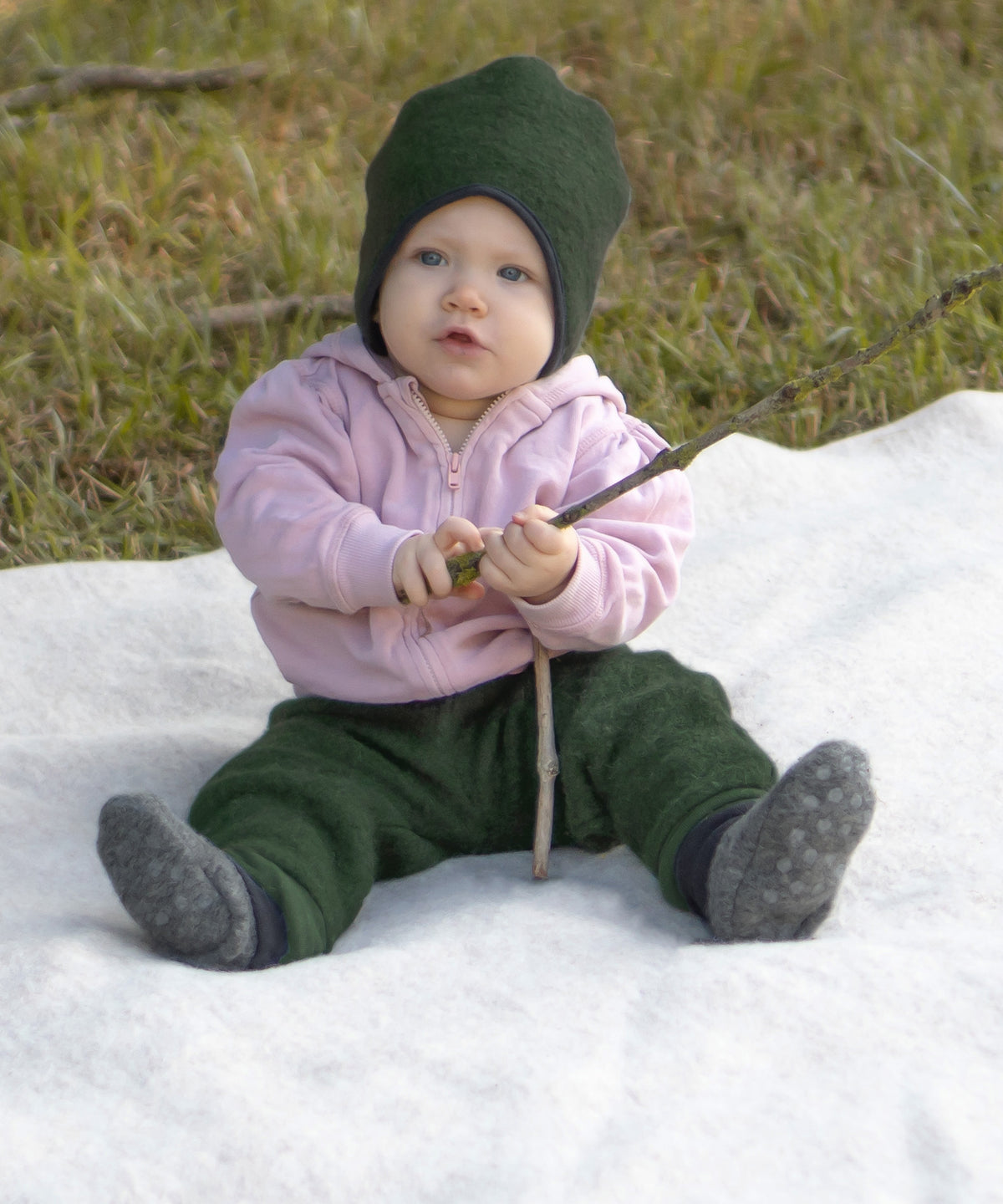 Baby sitzt auf einer Walkdecke und spielt mit einem Stock.
