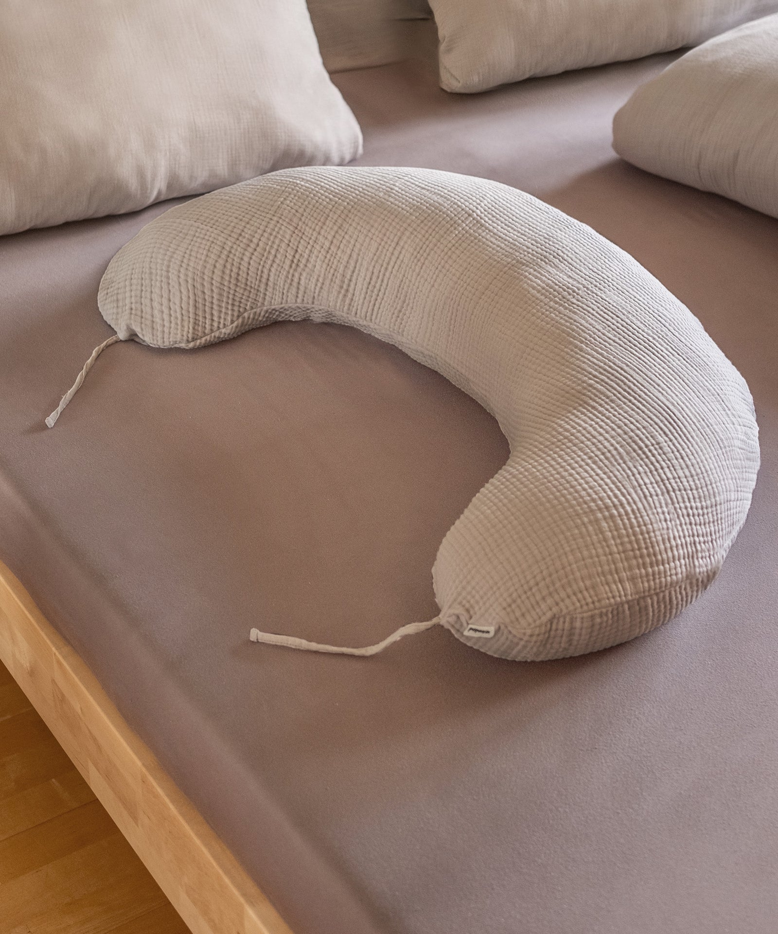 Allround-Talent Stilkissen*Schon während der Schwangerschaft kann das Stillkissen als Seitenschläferkissen oder Lagerungskissen unterstützend wirken.|Stillkissen mit Faserbällchen liegt auf Bett.