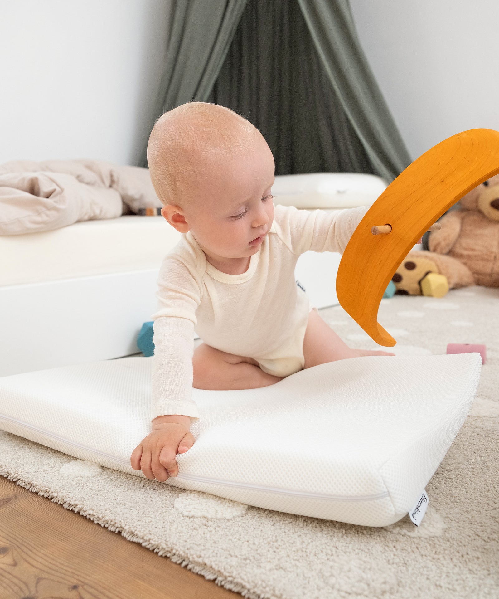 Fördert motorische Entwicklung|Baby stützt sich auf Keilkissen auf dem Boden.