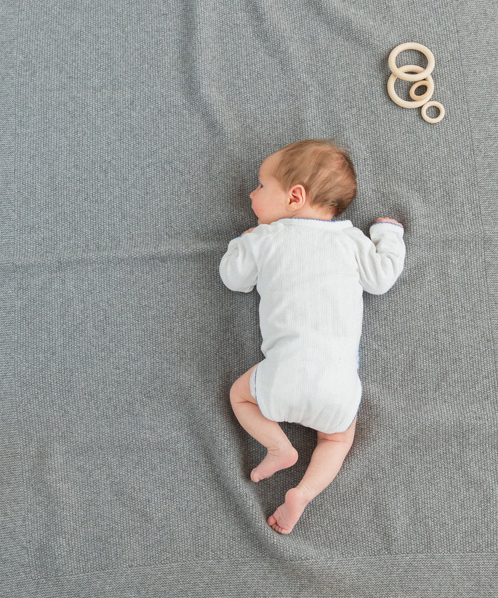 Angenehm warm*Durch die Wärme- und Feuchtigkeitsregulation unserer Decke haben es die Kleinen auch auf dem Boden warm und gemütlich.|Neugeborenes liegt auf grauer Lammwolldecke.