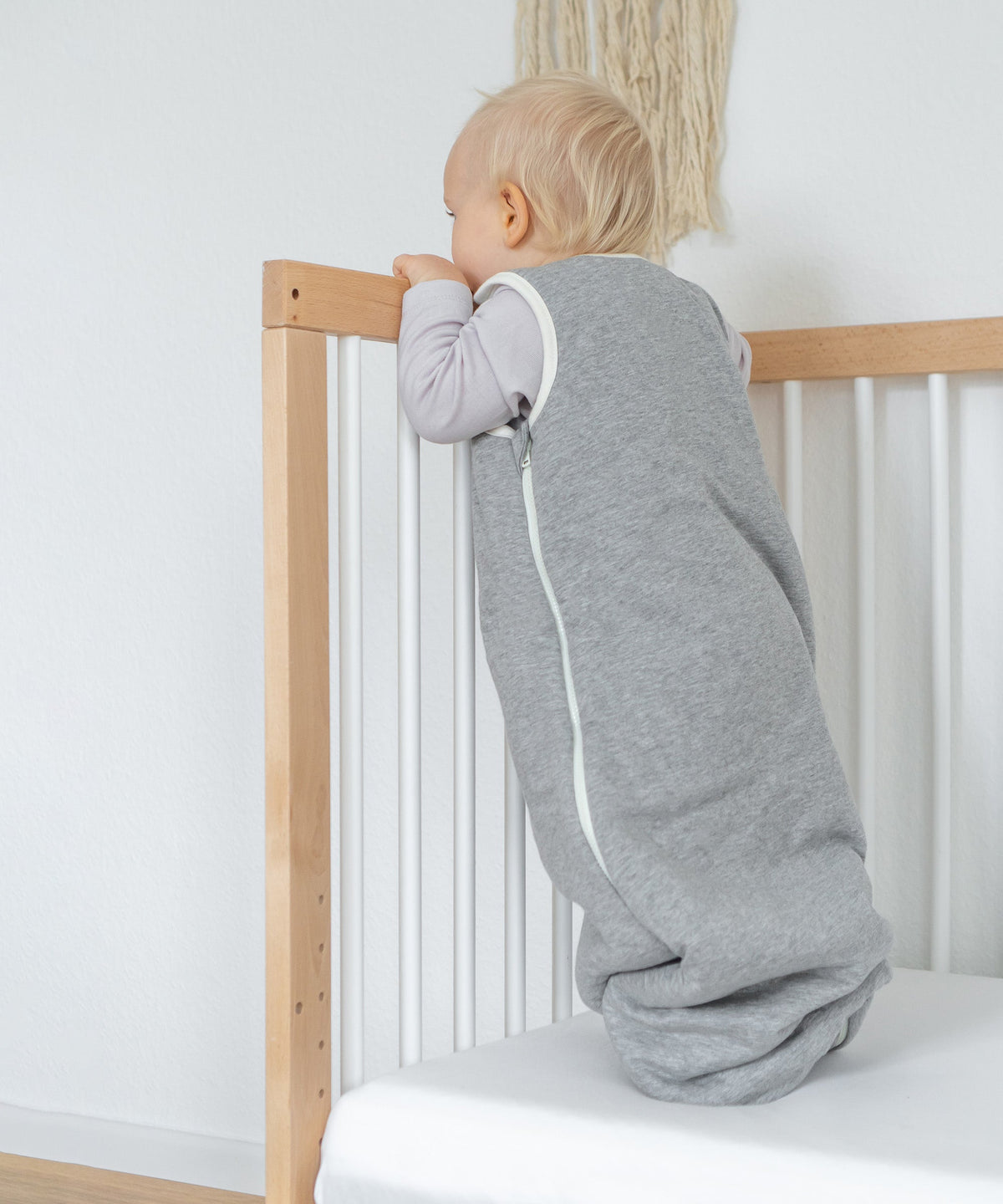 Baby trägt den Babyschlafsack und steht im Babybett.