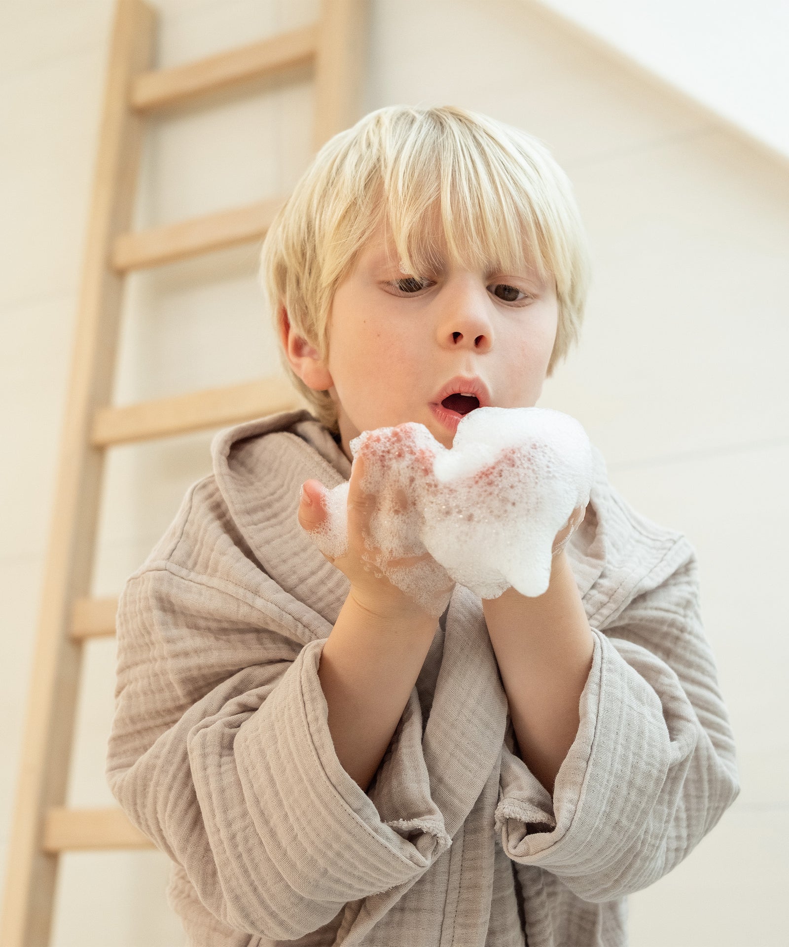 Kind mit Bademantel aus weichem Musselin spielt mit Schaum.
