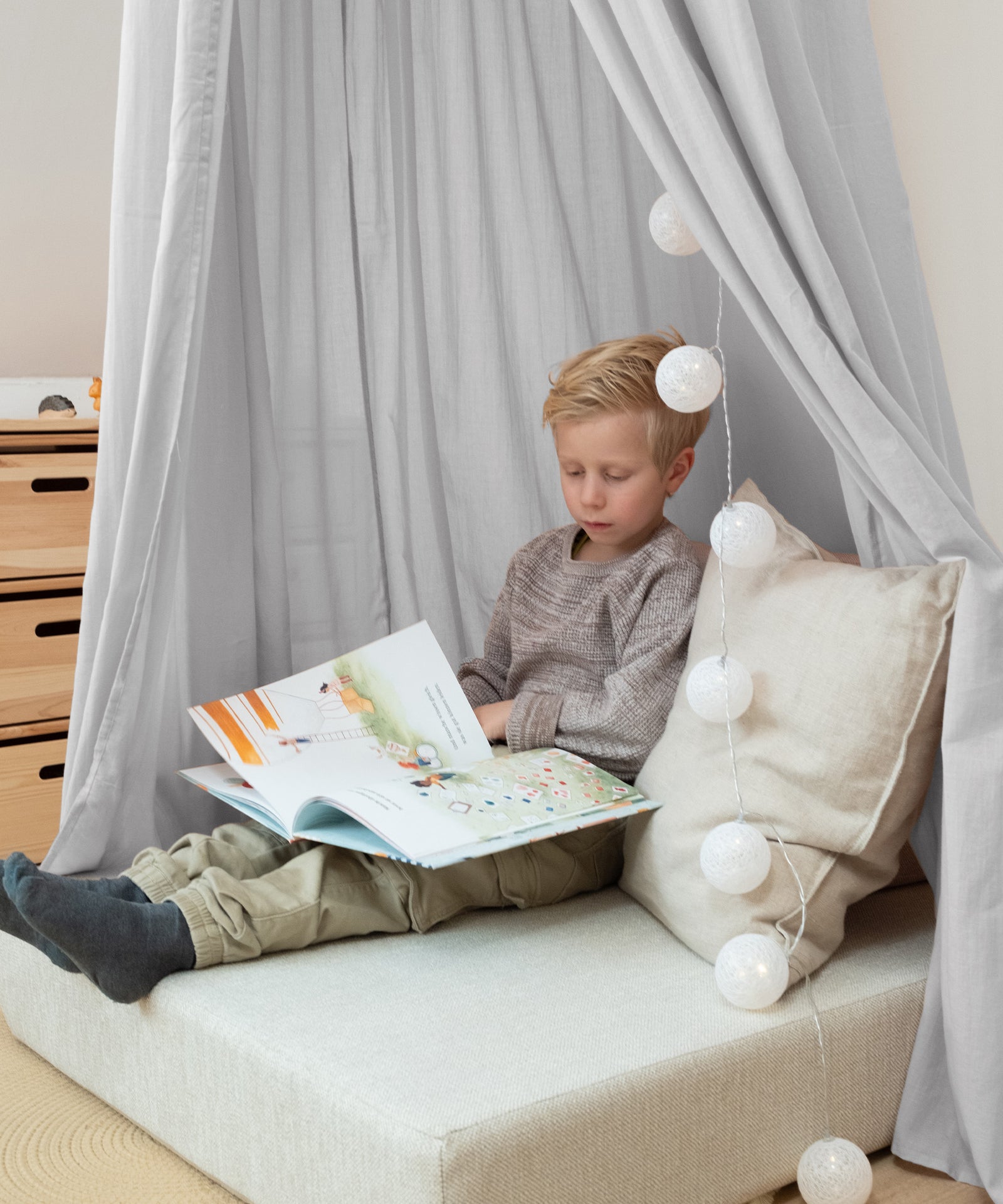 Gemütliche Kuschelecke mit grauem Baldachin und Lichterkette.