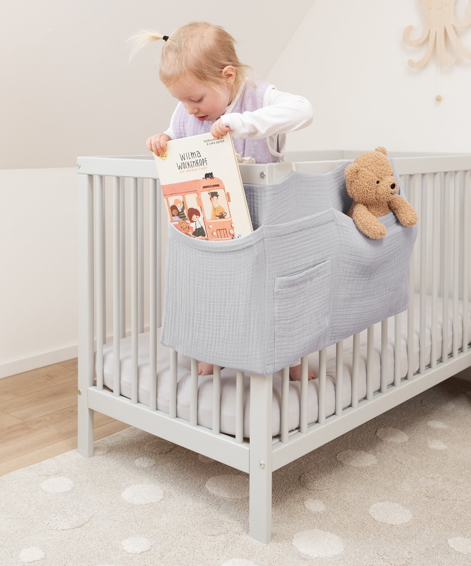 Selbstständig und sicher*Kinder greifen eigenständig auf Kuscheltiere oder Bücher zu. Der Organizer fördert Selbstständigkeit und bleibt sicher befestigt.|Kind holt ein Buch aus dem Bett Organizer.
