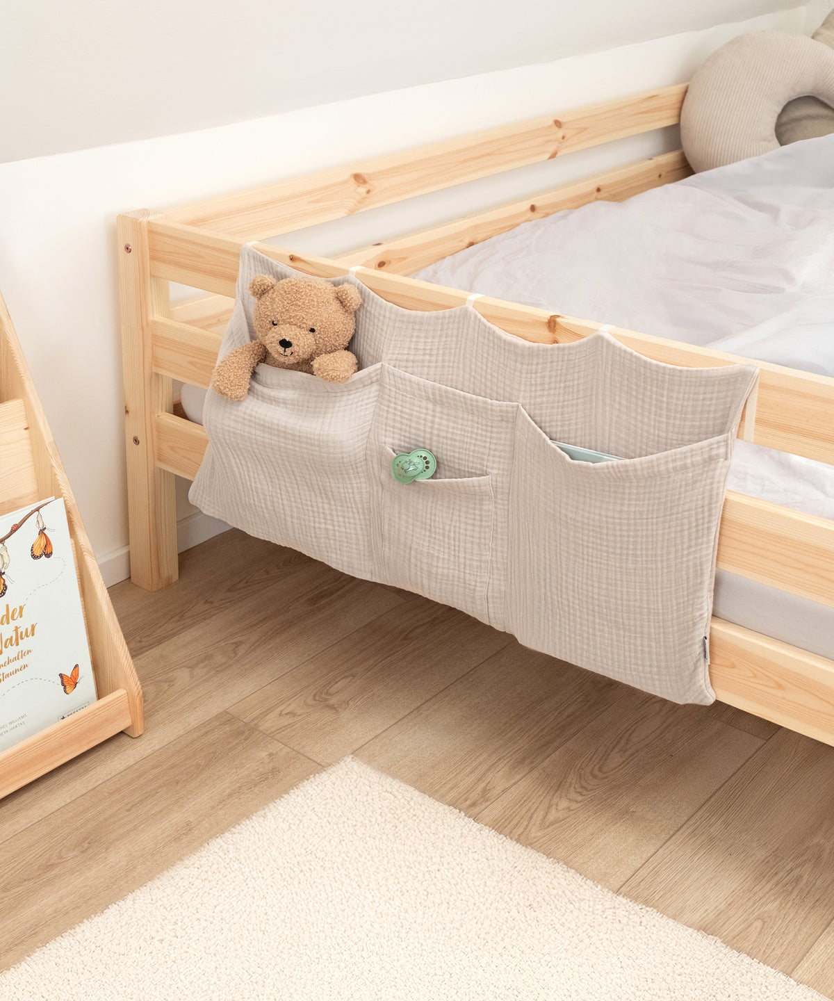 Bett Organizer in Beige am Kinderbett mit Kuscheltier und Schnuller in den Taschen.
