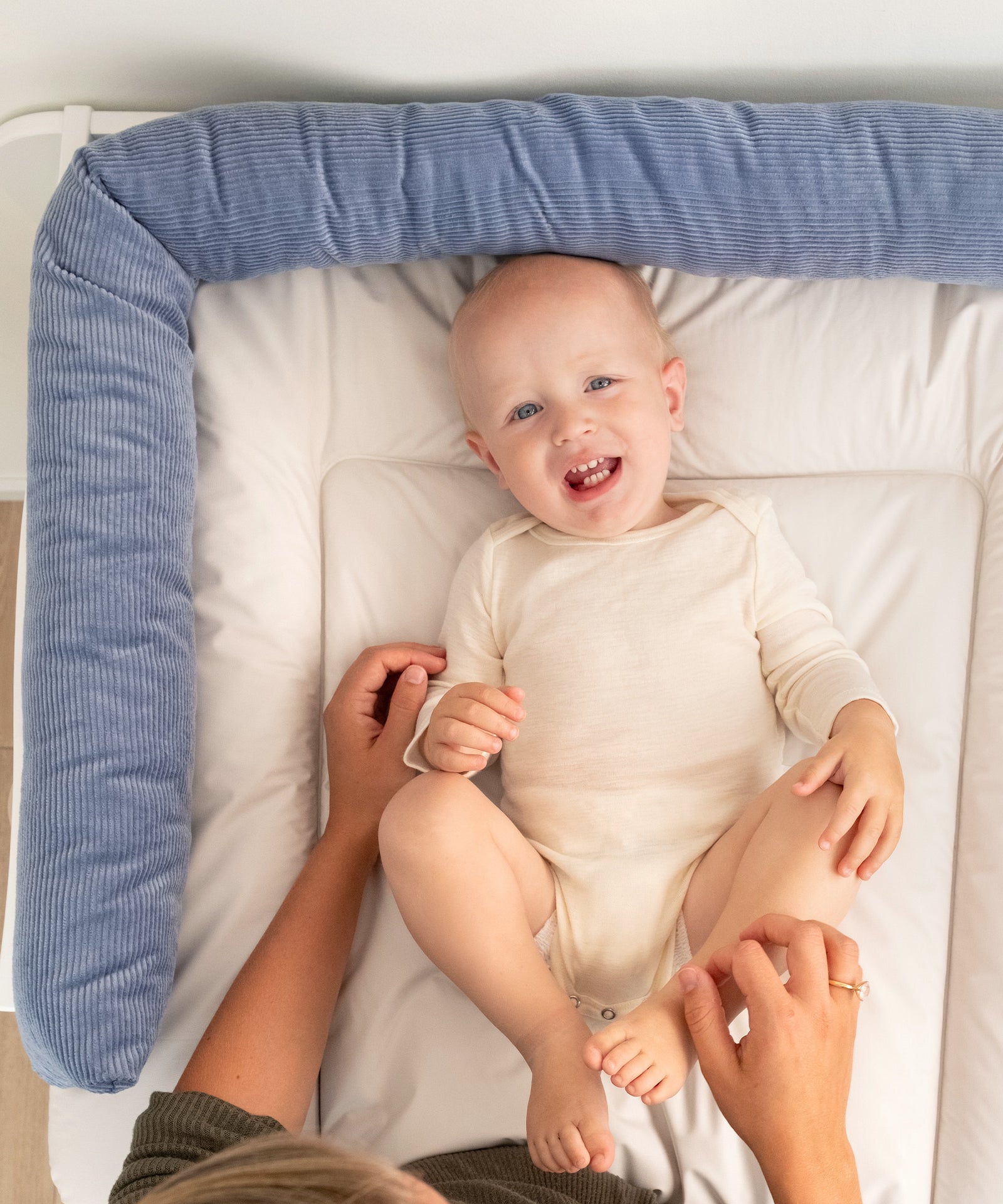 Flexibel im Alltag einsetzbar*Ob im Babybett, auf dem Sofa oder Wickeltisch – die Bettschlange ist ein echter Allrounder im Familienalltag.|Baby liegt auf dem Wickeltisch, am Rand rundherum liegt die Bettschlange in jeansblau.