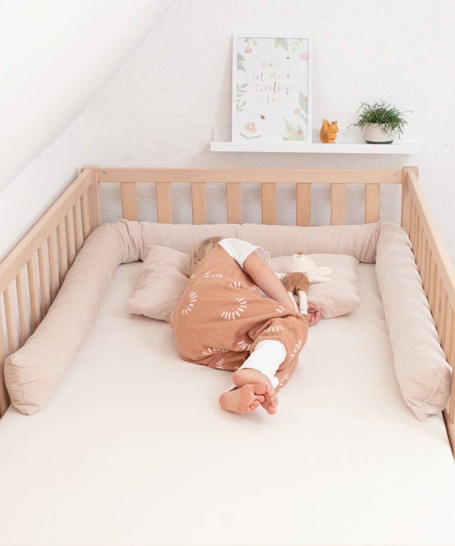 Kuschelig & formstabil*Dank ihrer weichen Füllung bleibt die Bettschlange formstabil – für langanhaltenden Komfort & sicheren Halt.|Kind liegt im Kinderbett umrandet von einer Bettschlange in Beige.