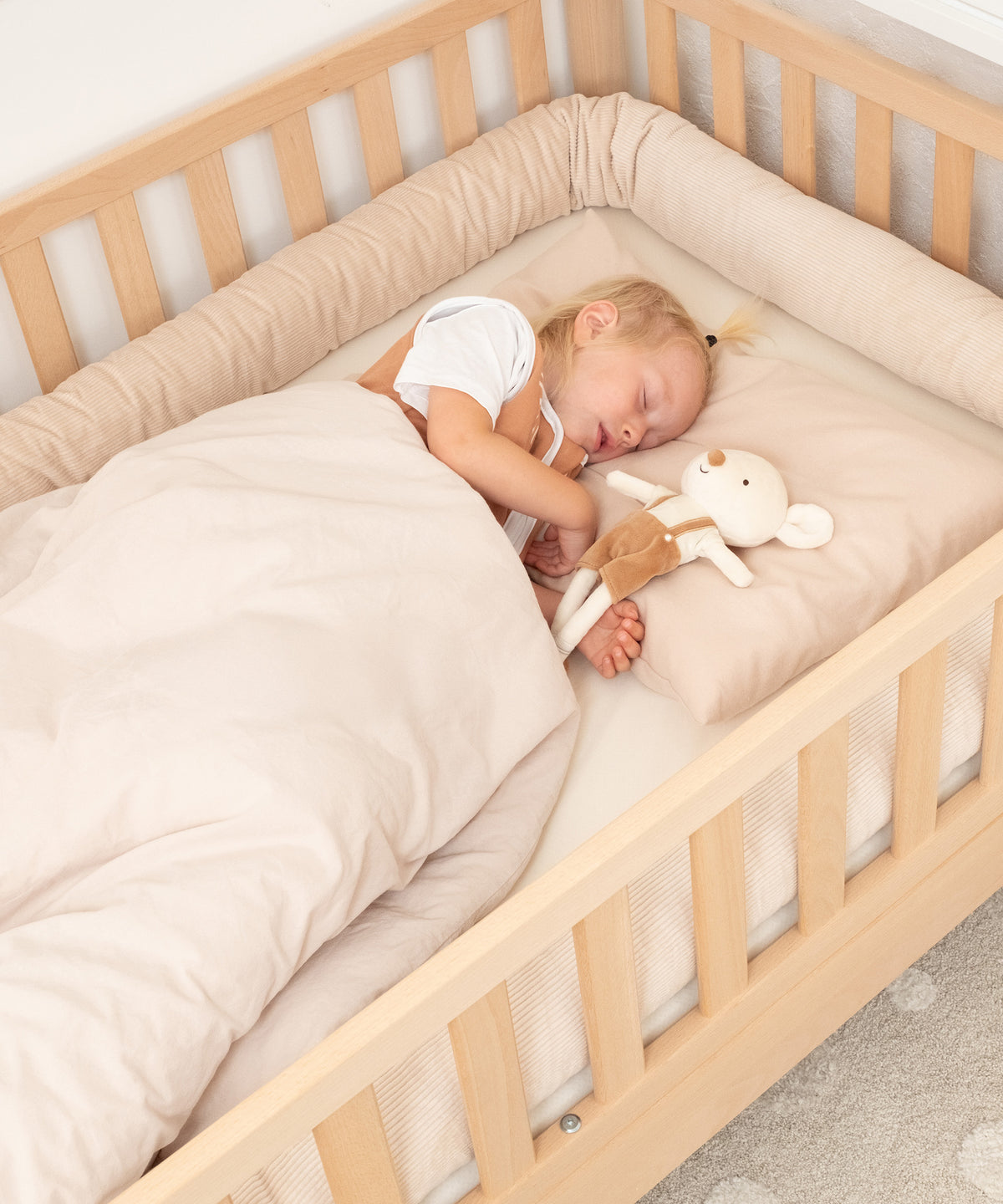 Kind schläft im Kinderbett mit Bettschlange in Beige.
