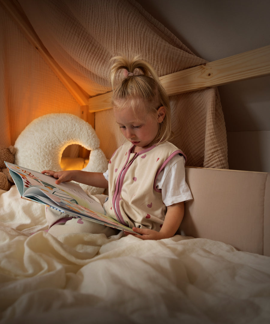 Gemütliche Kuschelecke*Die weich gepolsterte Bettumrandung sorgt für Gemütlichkeit im Bett.| Kind liest im Bett und im Hintergrund ist die Bettumrandung am Kinderbett befestigt.
