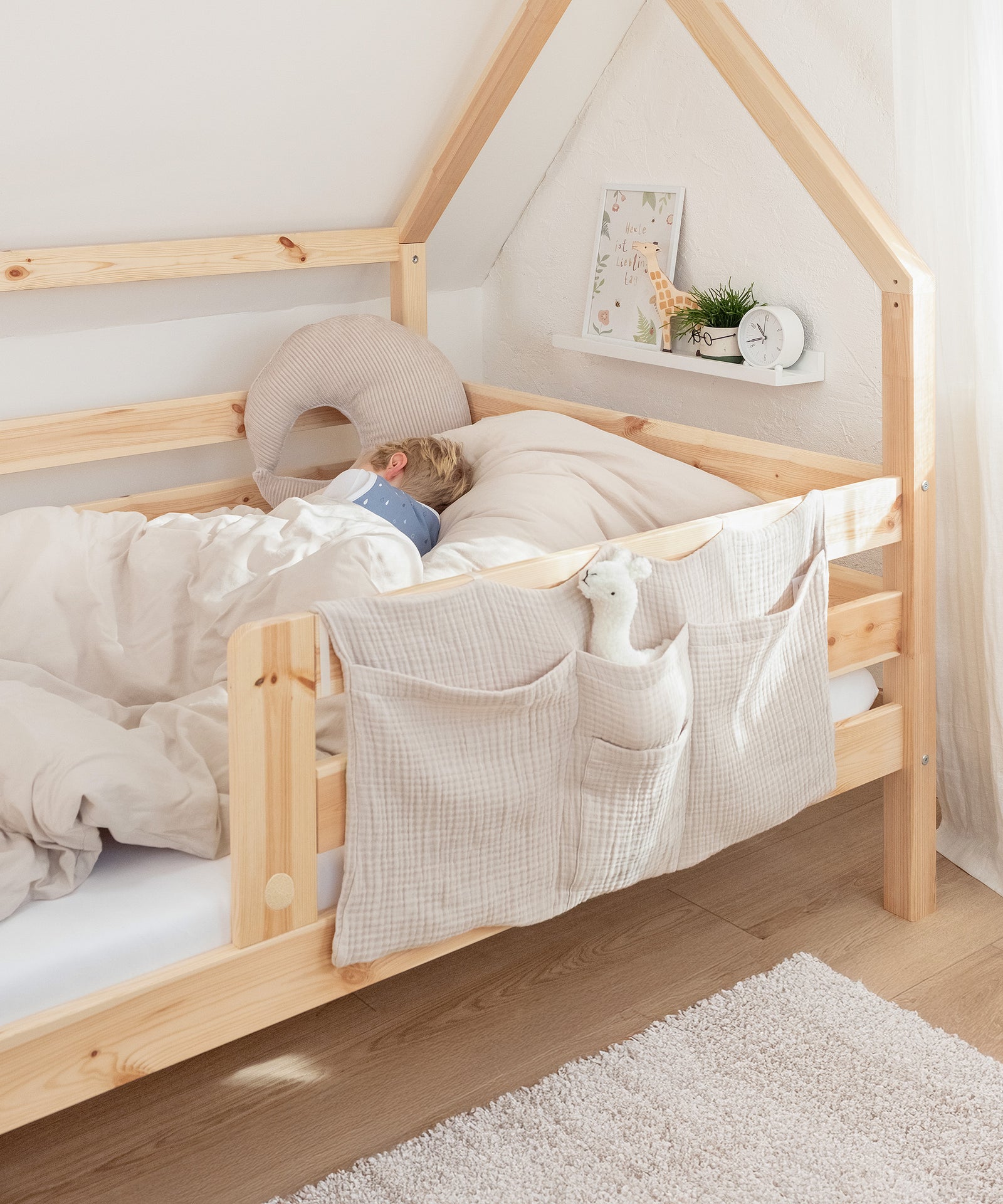 Abnehmbarer Rausfallschutz*Mit dem abnehmbaren Rausfallschutz schläft dein Kind von Anfang an sicher und geschützt.|Kind liegt in dem Bett, vorne dran ist der Rausfallschutz befestigt.