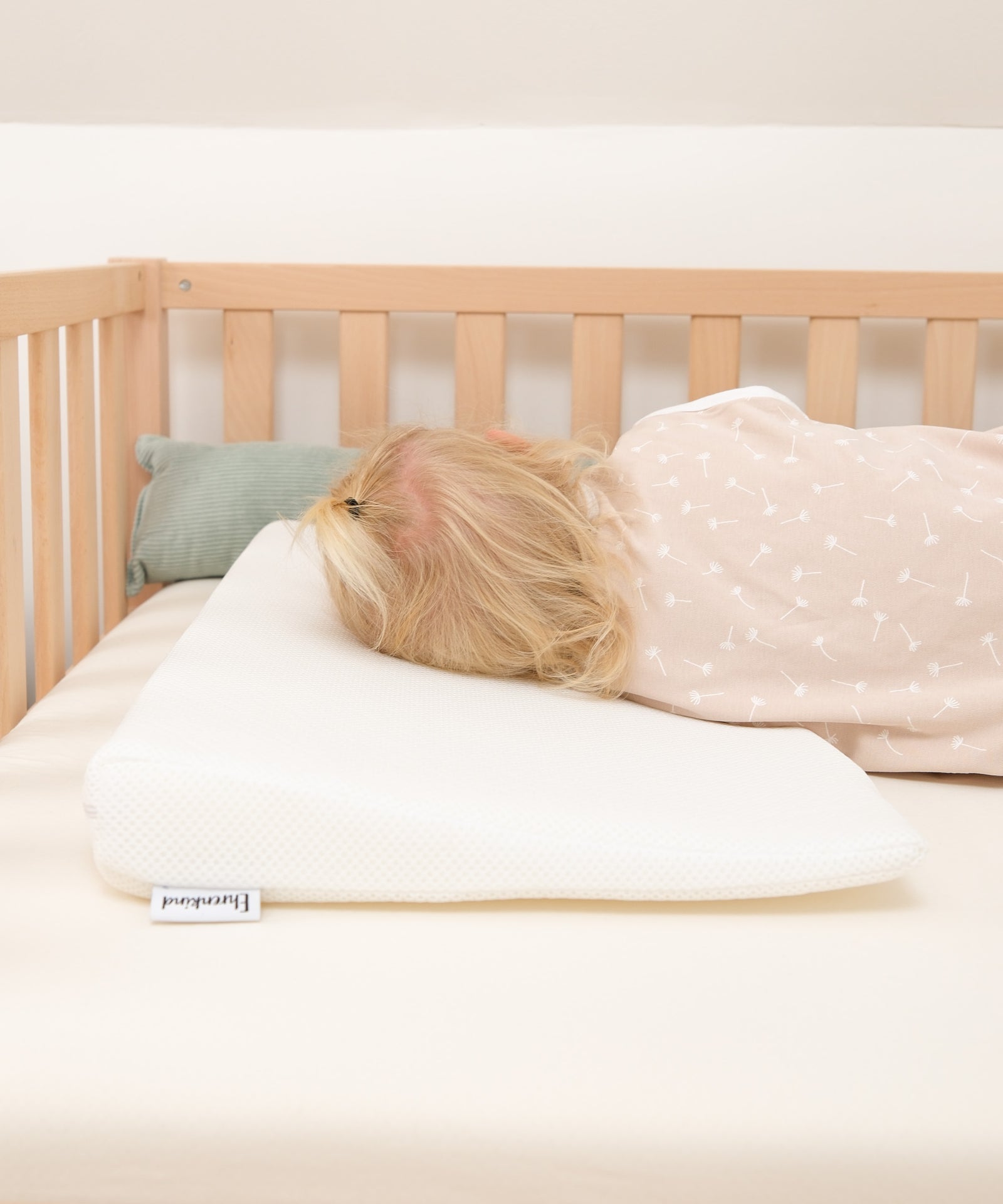 Kind schläft auf Keilkissen im Bett.